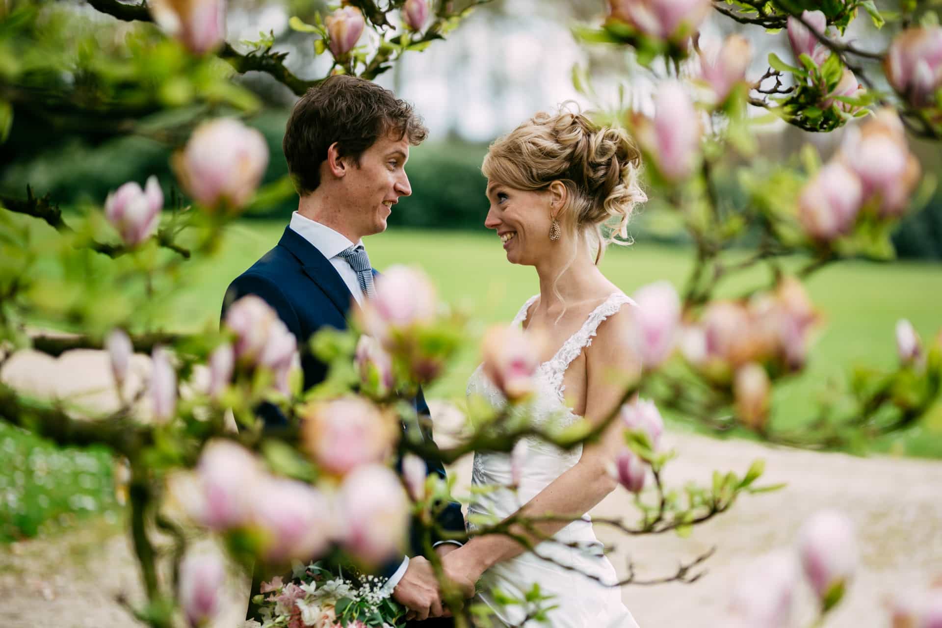 Een bruid en bruidegom staan onder een magnoliaboom, waardoor een prachtige bruiloftsthema-sfeer ontstaat.