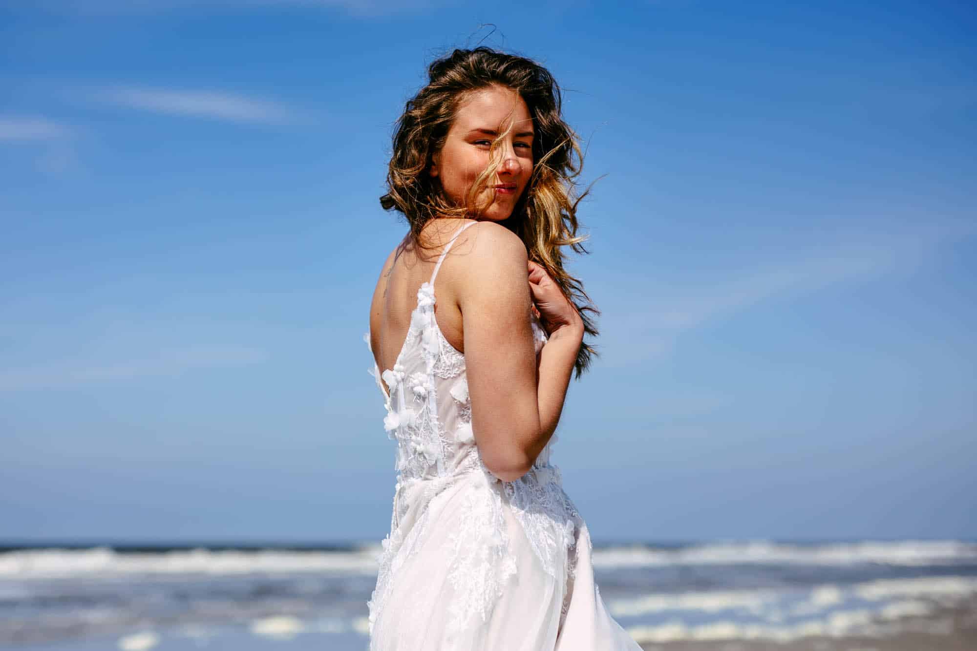 Half totaal foto van een bruid met een goedkope trouwjurk op het strand met haar haren in het gezicht.