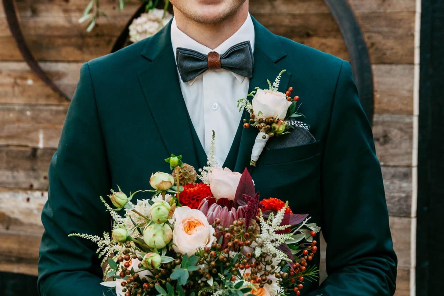 A groom in a green suit with a corsage bouquet.