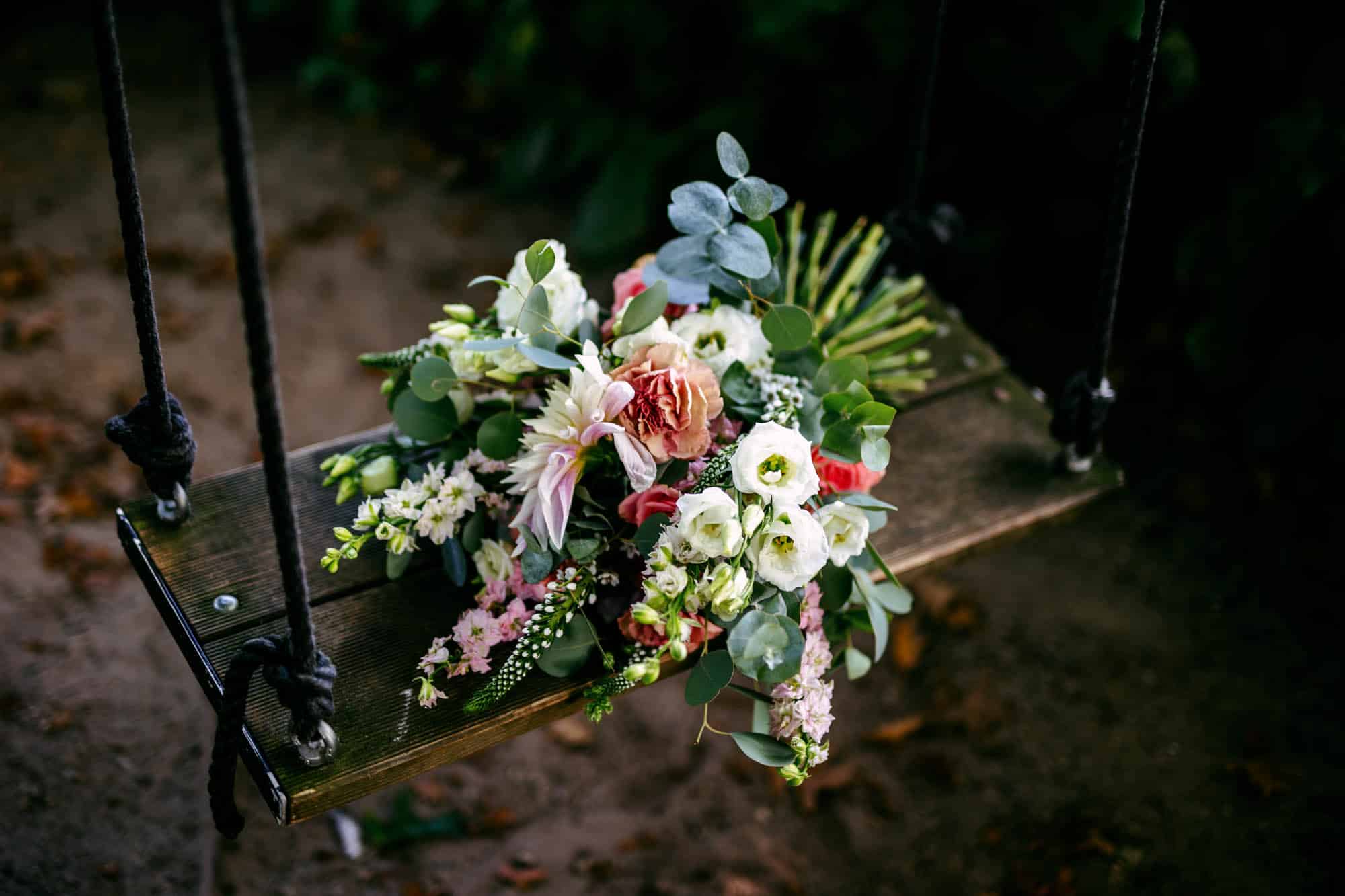 A wedding bouquet stands on a wooden swing.