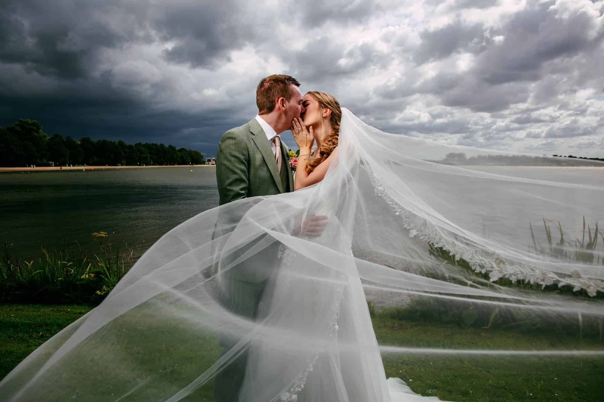 Een bruid en bruidegom delen op hun trouwdag een hartstochtelijke kus onder een stormachtige hemel en omarmen de betoverende sfeer van regen op je bruiloft.