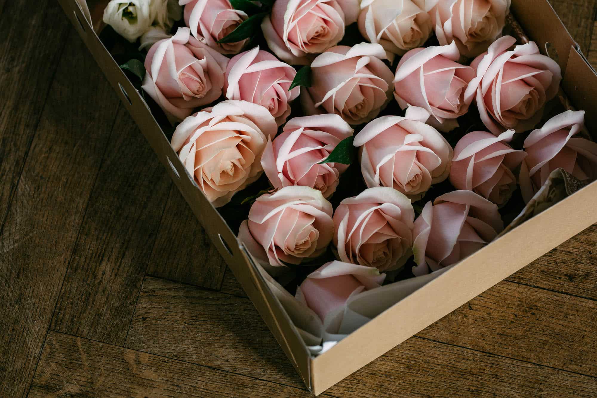 Roze en witte rozen in een doos op een houten vloer die de delicate schoonheid van bloemen laat zien.