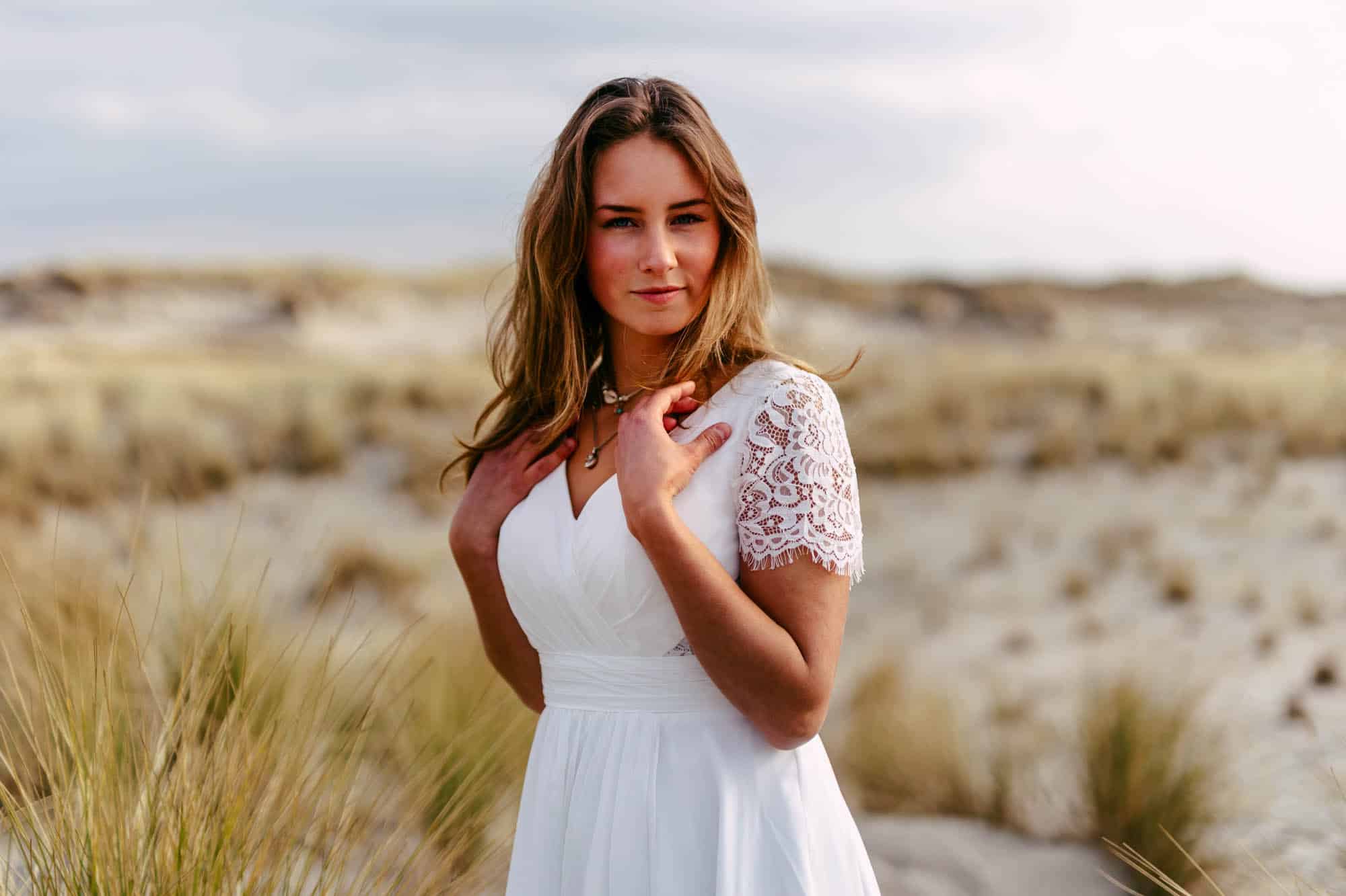 Een mooie vrouw in een witte trouwjurk staande in het zand.