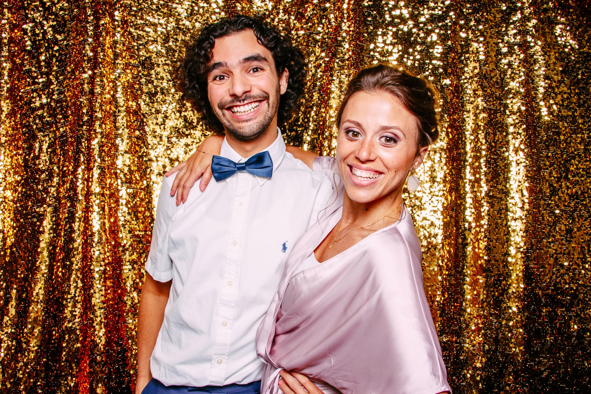 A casually chic man and woman pose for a photo against a gold background.