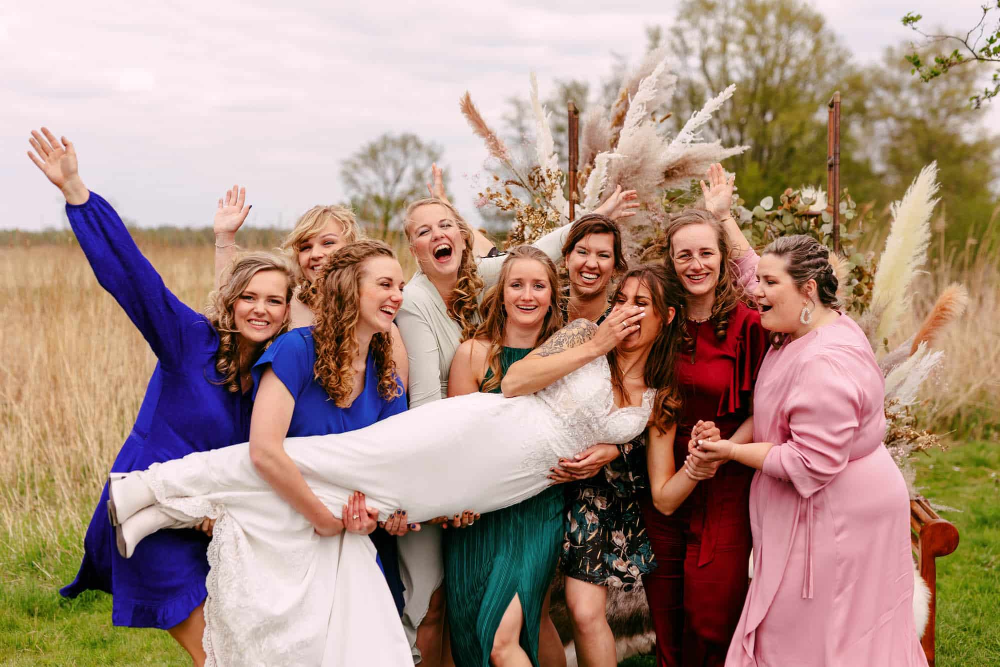 Een groep bruidsmeisjes gekleed in casual chique outfits poseren voor een foto in een veld.