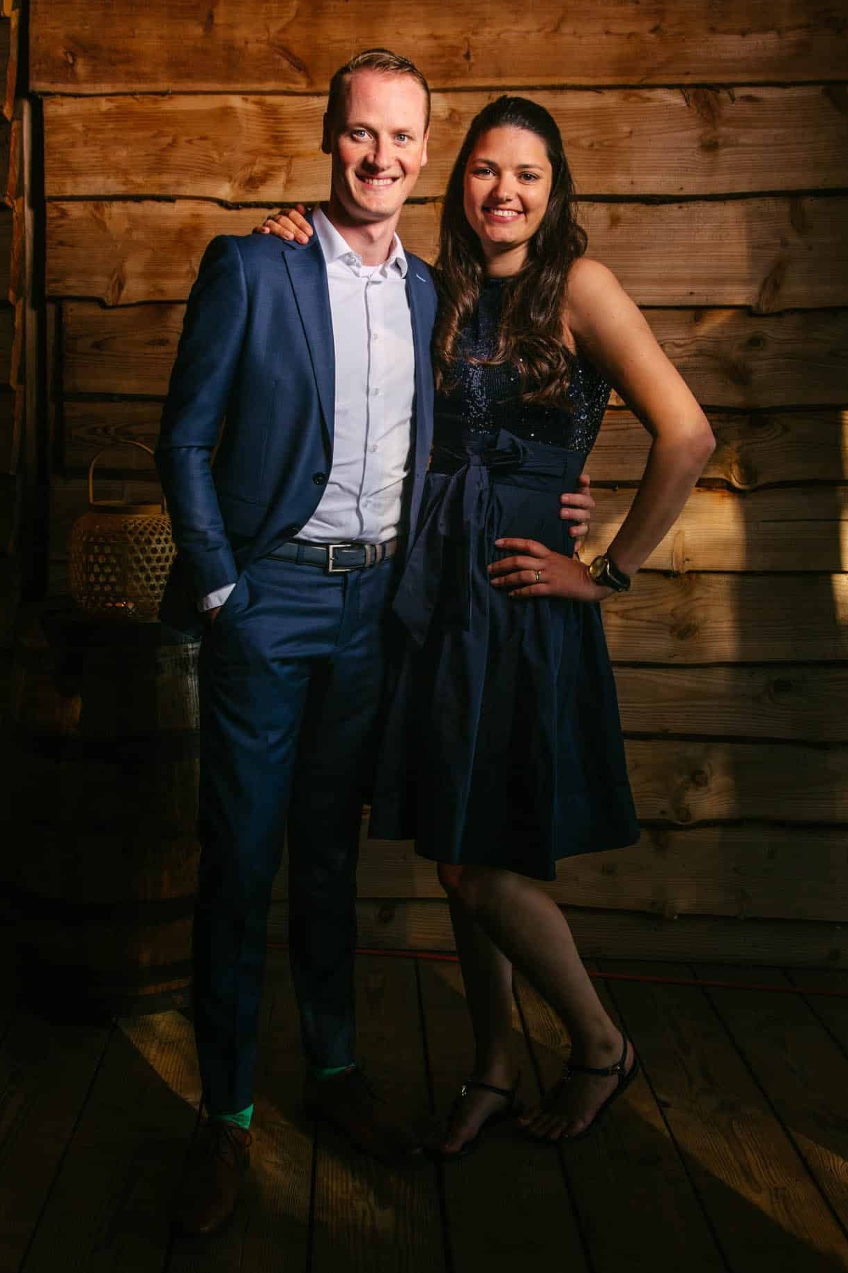 A couple dressed in Tenue de ville pose for a photo in front of a wooden wall.