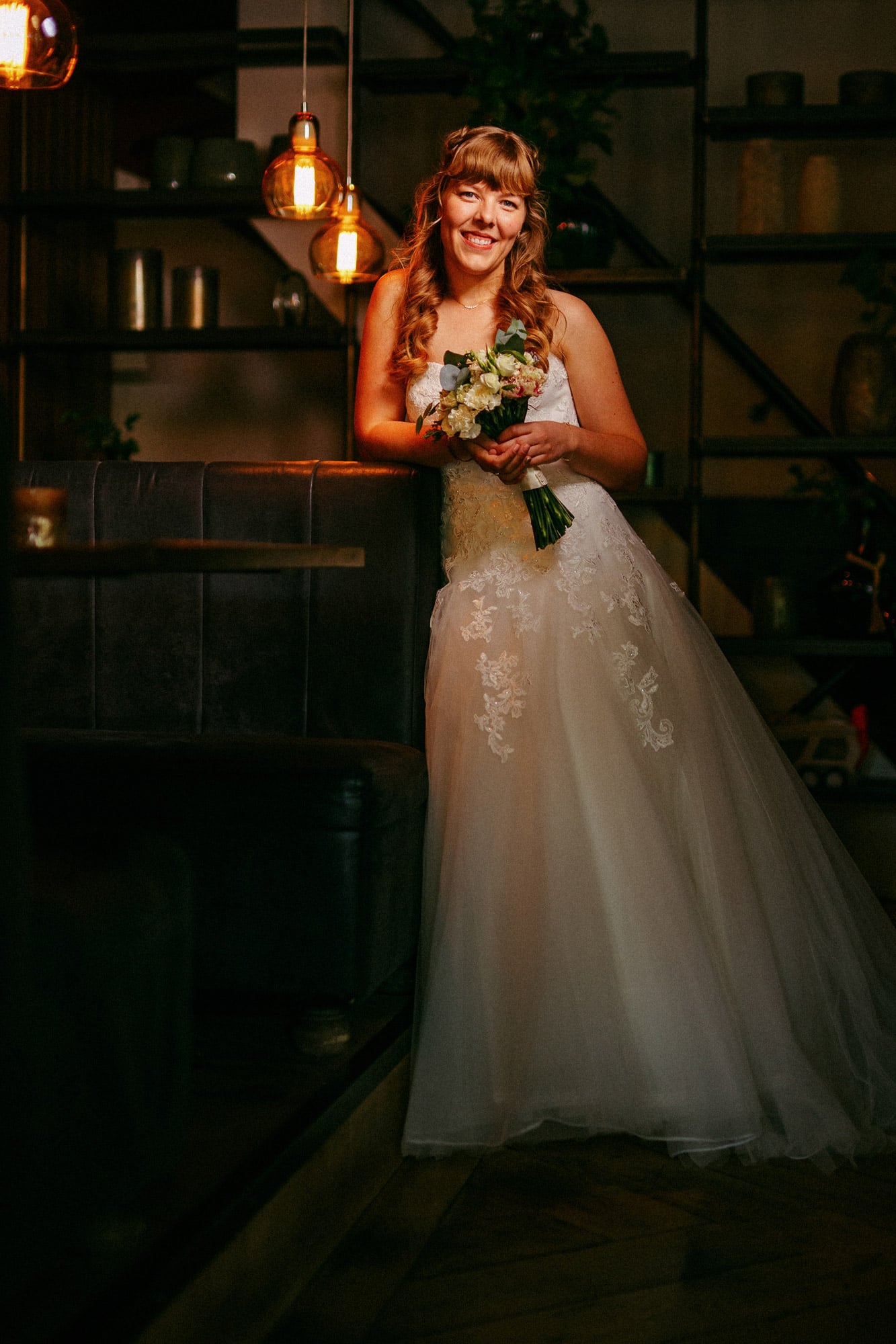 A bride poses for a photo with her beautiful Wedding Bouquet in a dimly lit room.