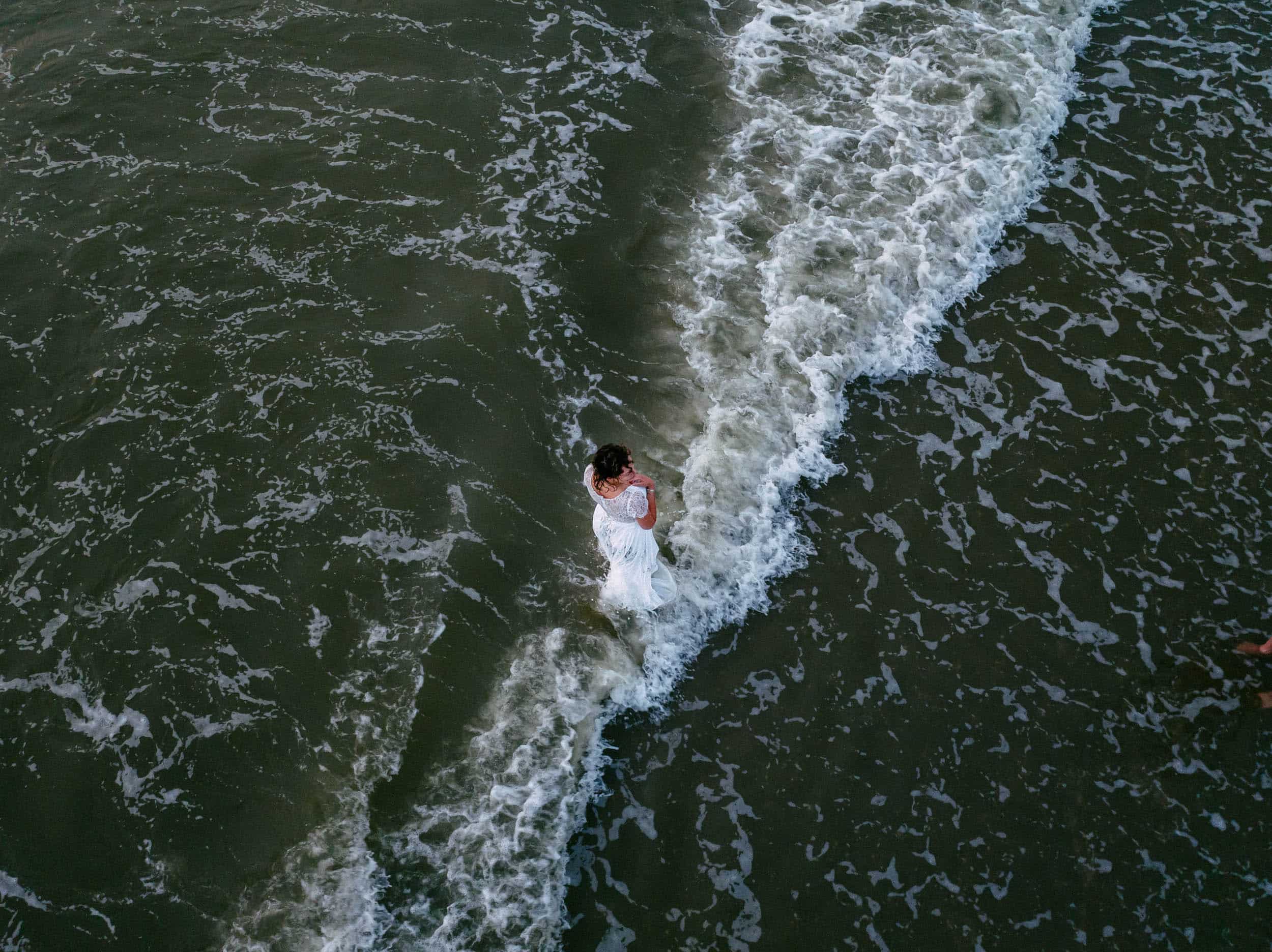 An aerial view of a bride and groom in the ocean during their Trash The Dress session.