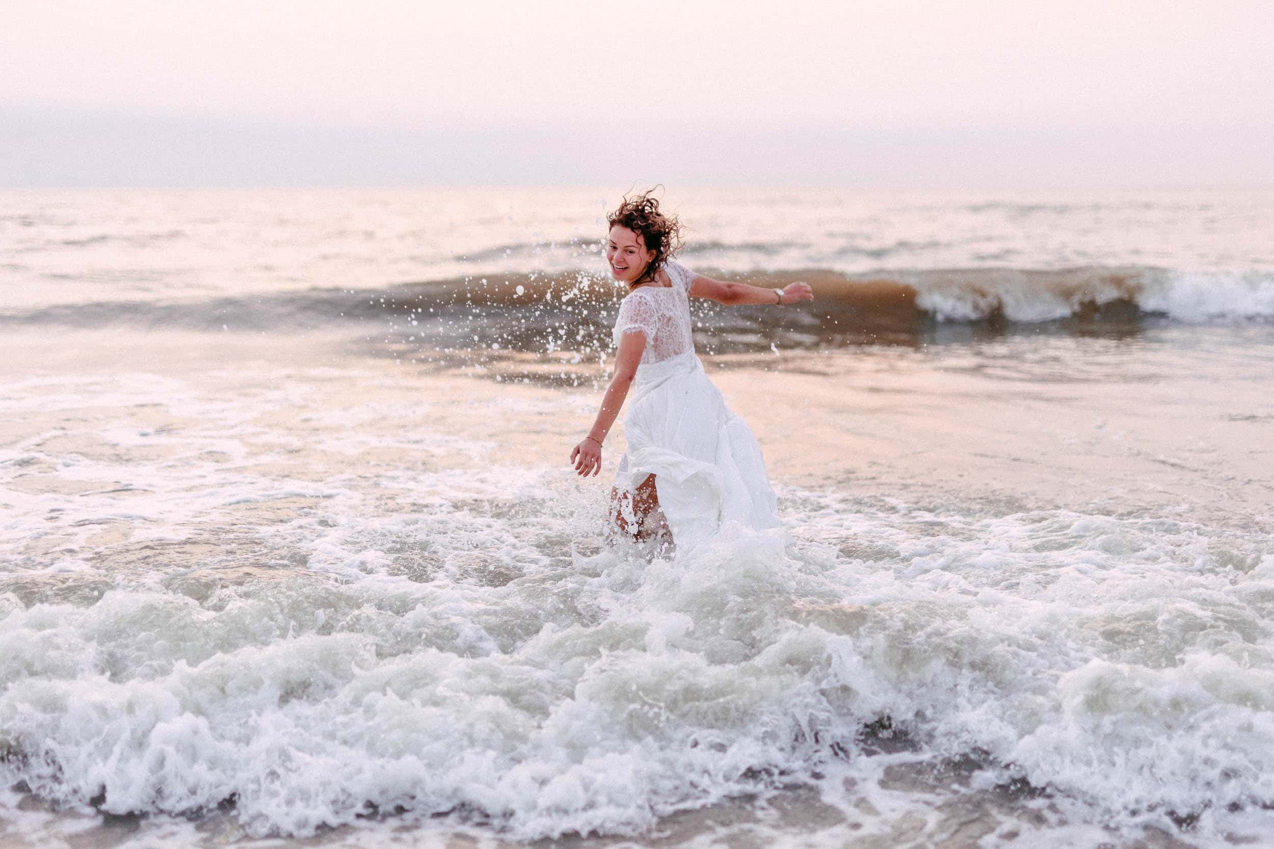 Een vrouw in een witte jurk die het concept van "Trash The Dress" omarmt door zichzelf onbevreesd in de oceaan onder te dompelen.