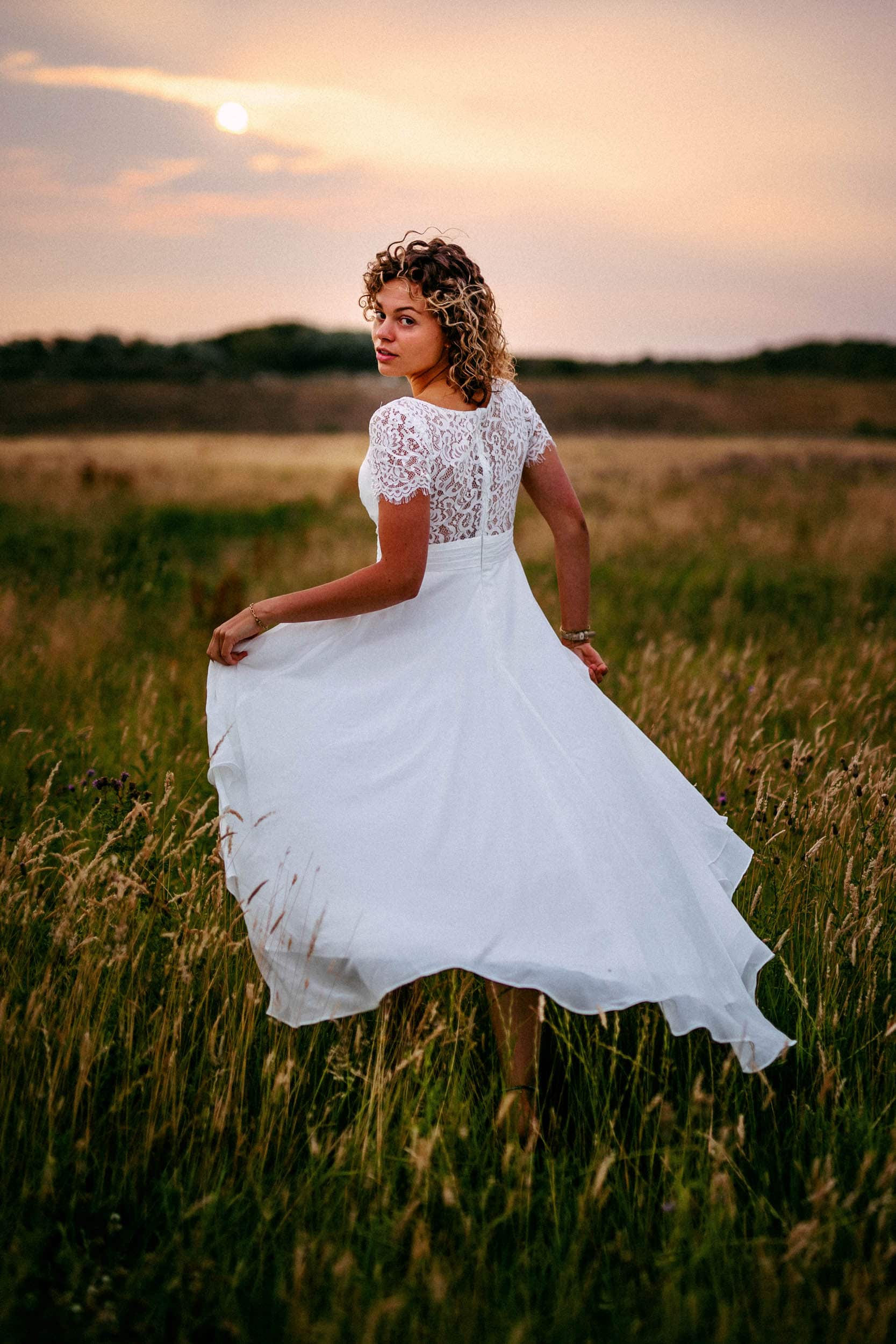 A Trash The Dress session with a woman in a white dress standing gracefully amid a picturesque field.