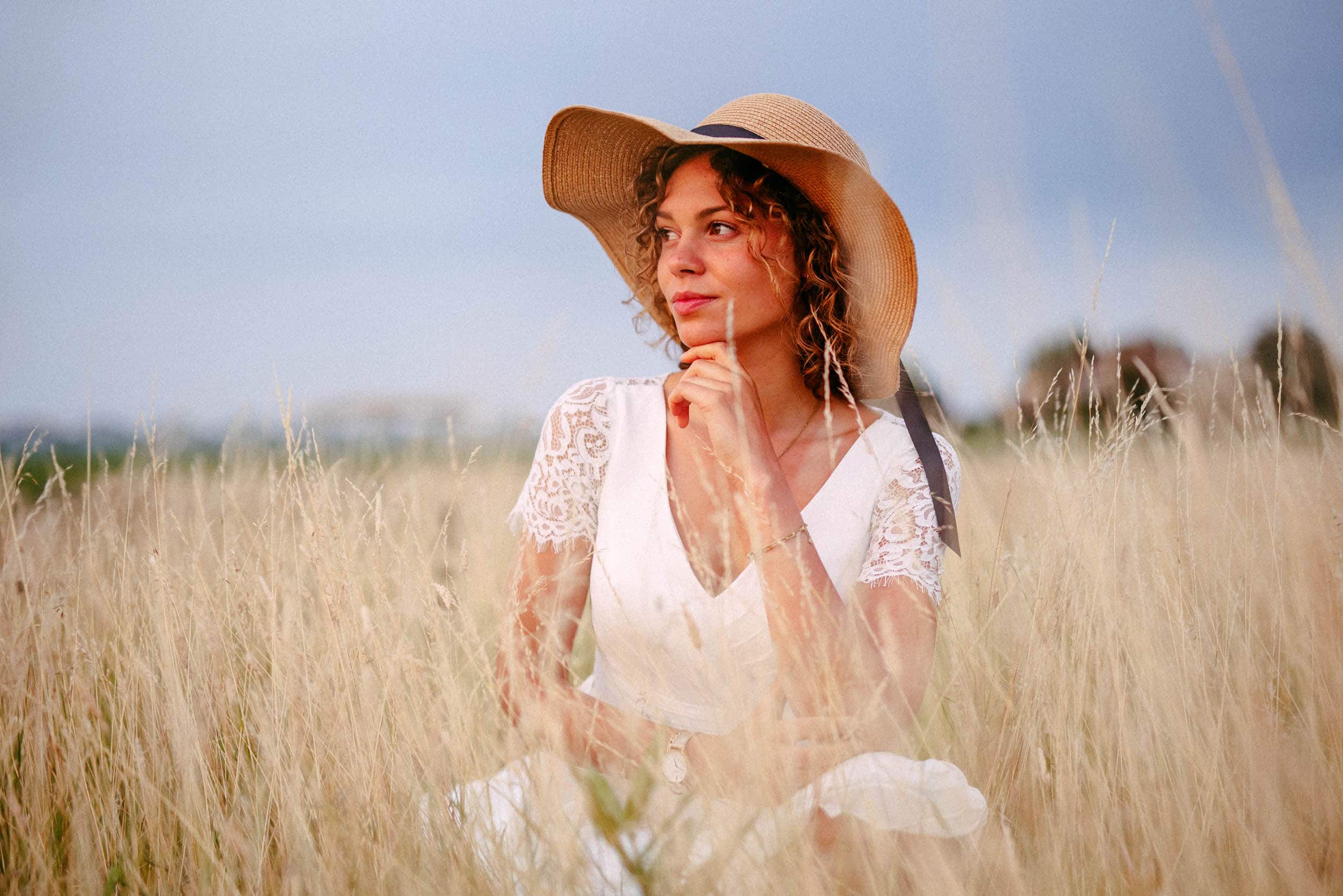 Een vrouw met hoed, zittend in een veld tijdens ondertrouw.