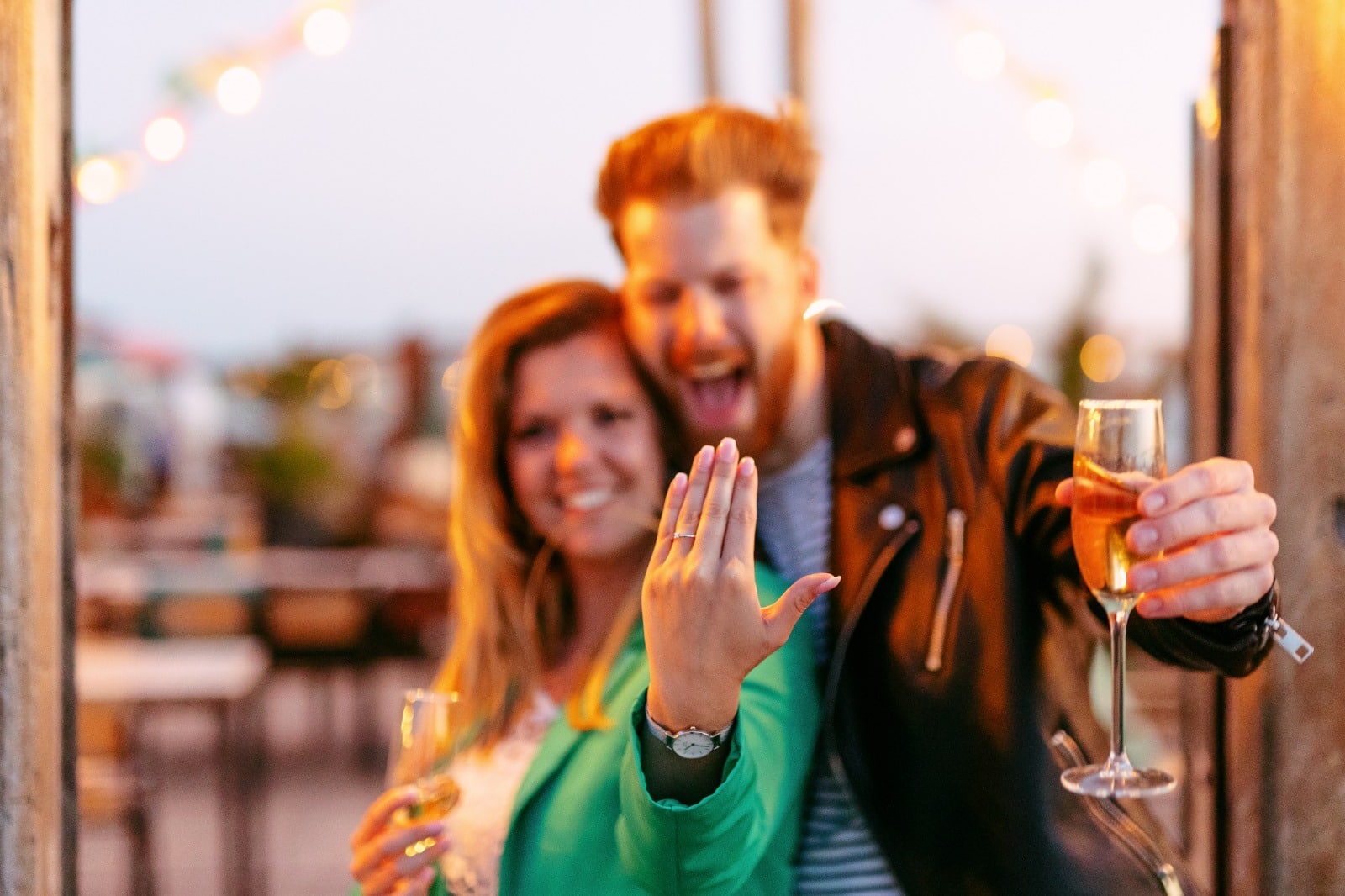 A man and woman hold champagne glasses at an outdoor wedding where they have just become engaged.