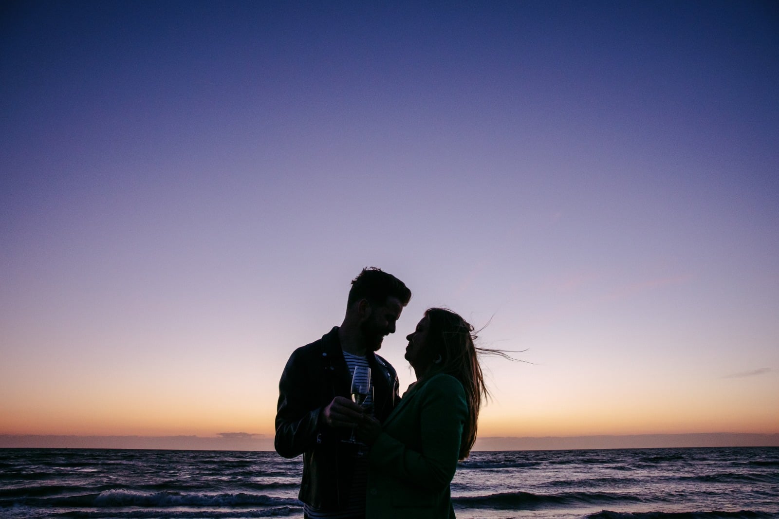 Een romantisch silhouet van een stel dat bij zonsondergang op het strand staat.