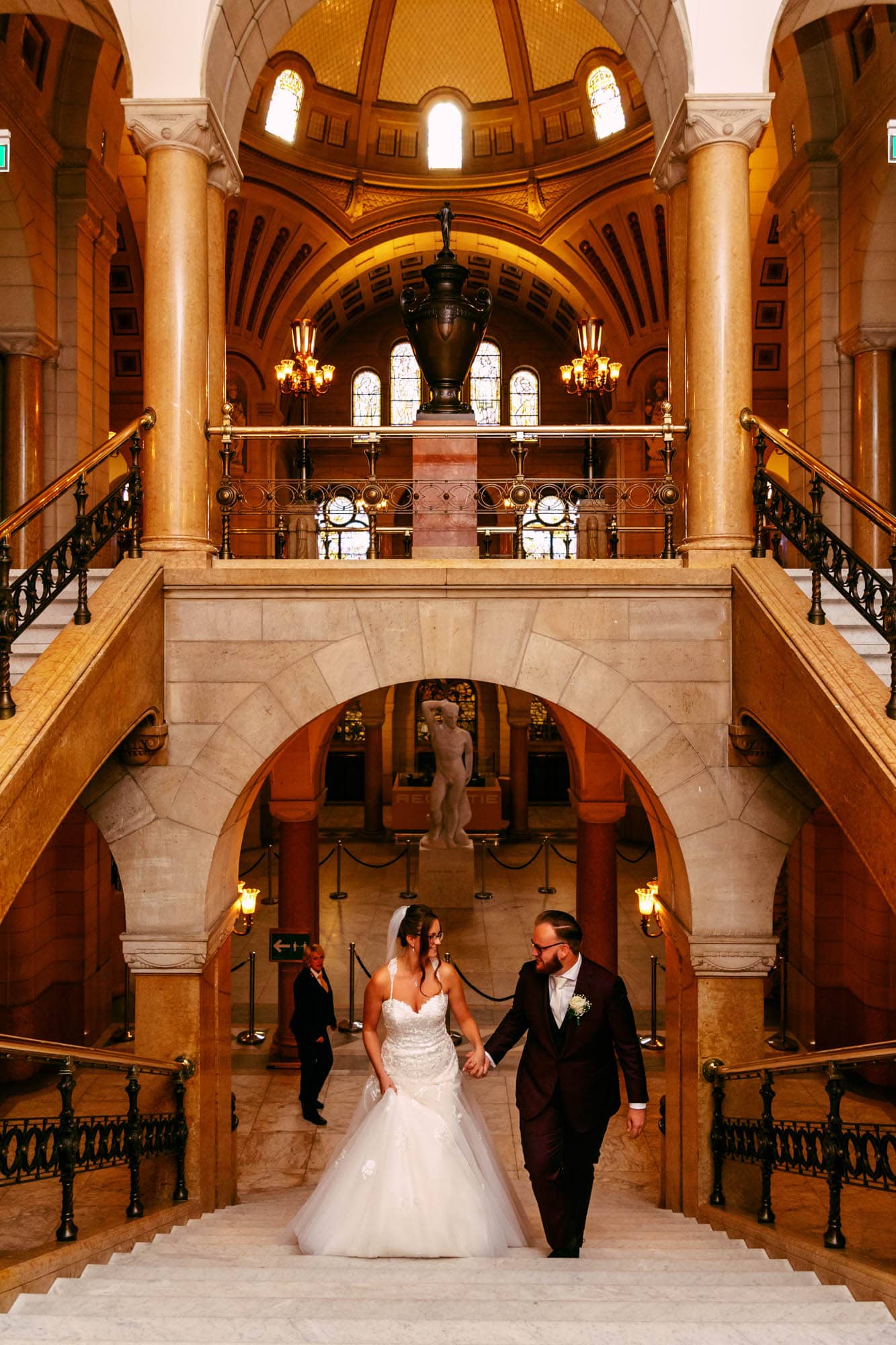 Getting married in Rotterdam - A bride and groom gracefully descend the stairs in a beautiful building.
