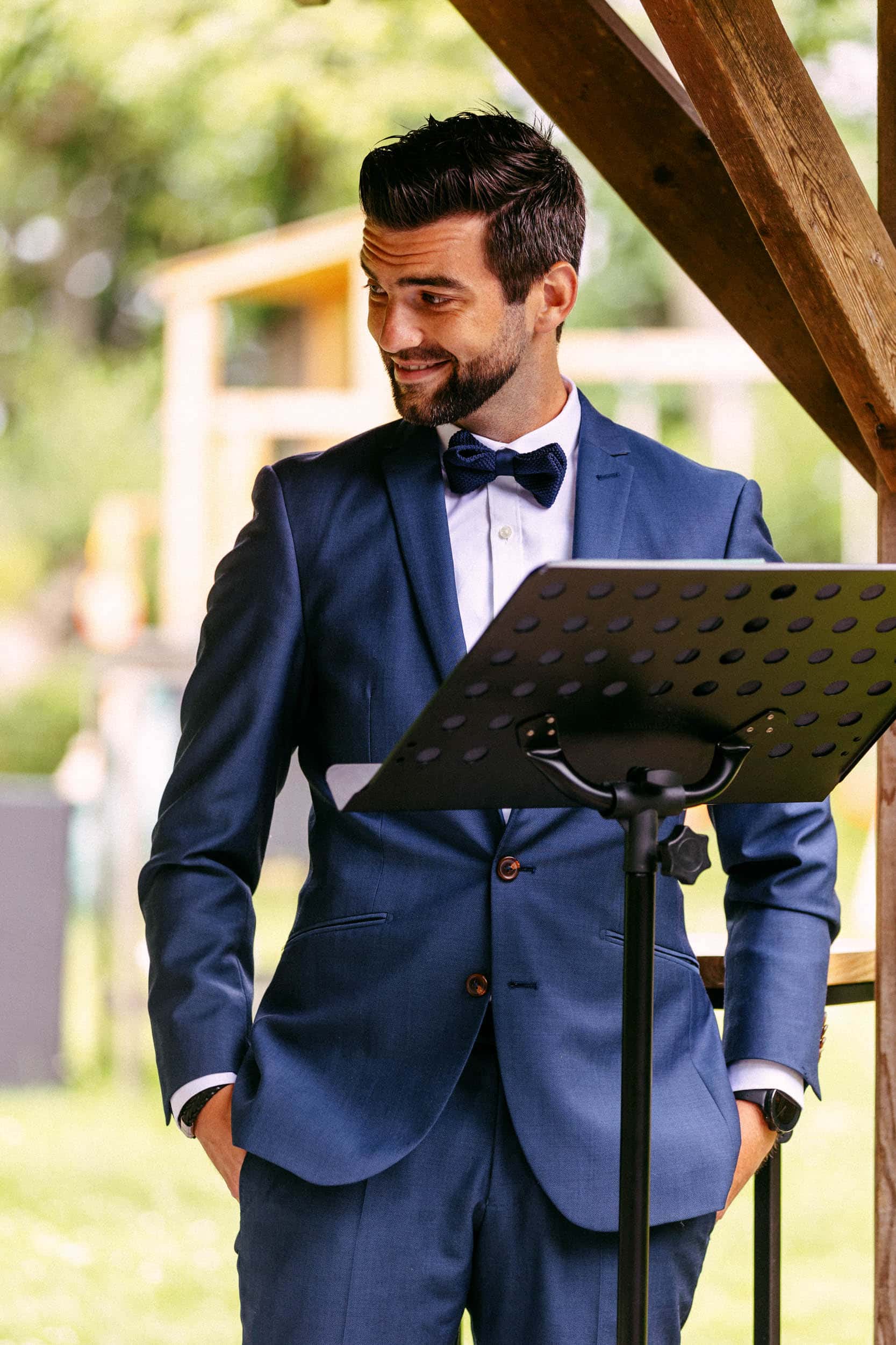 A man in a suit delivers a ready-made speech next to a music stand at a wedding.