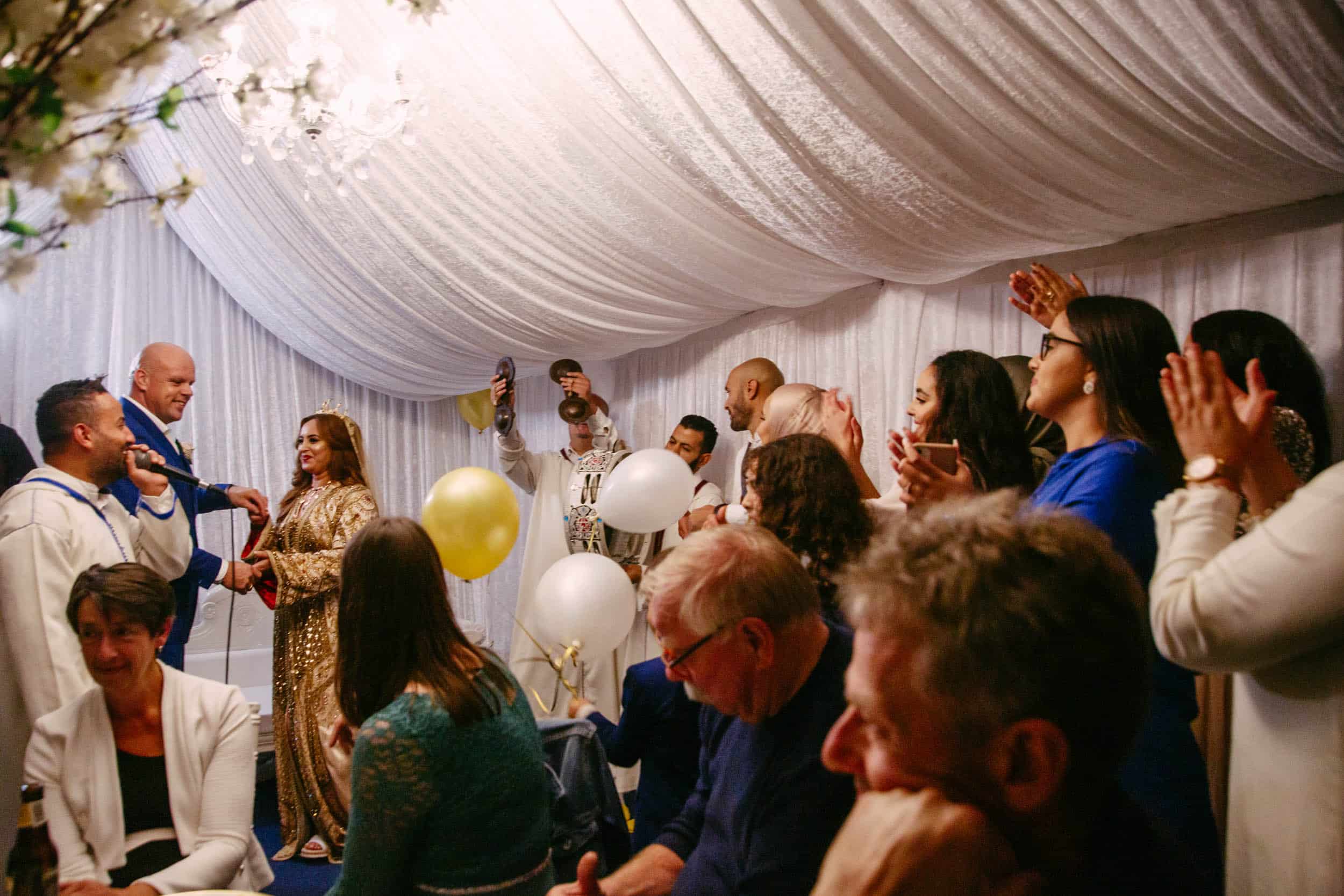 Beschrijving: Een bruiloftsceremonie in een tent met mensen die applaudisseren in het thema van de bruiloft.