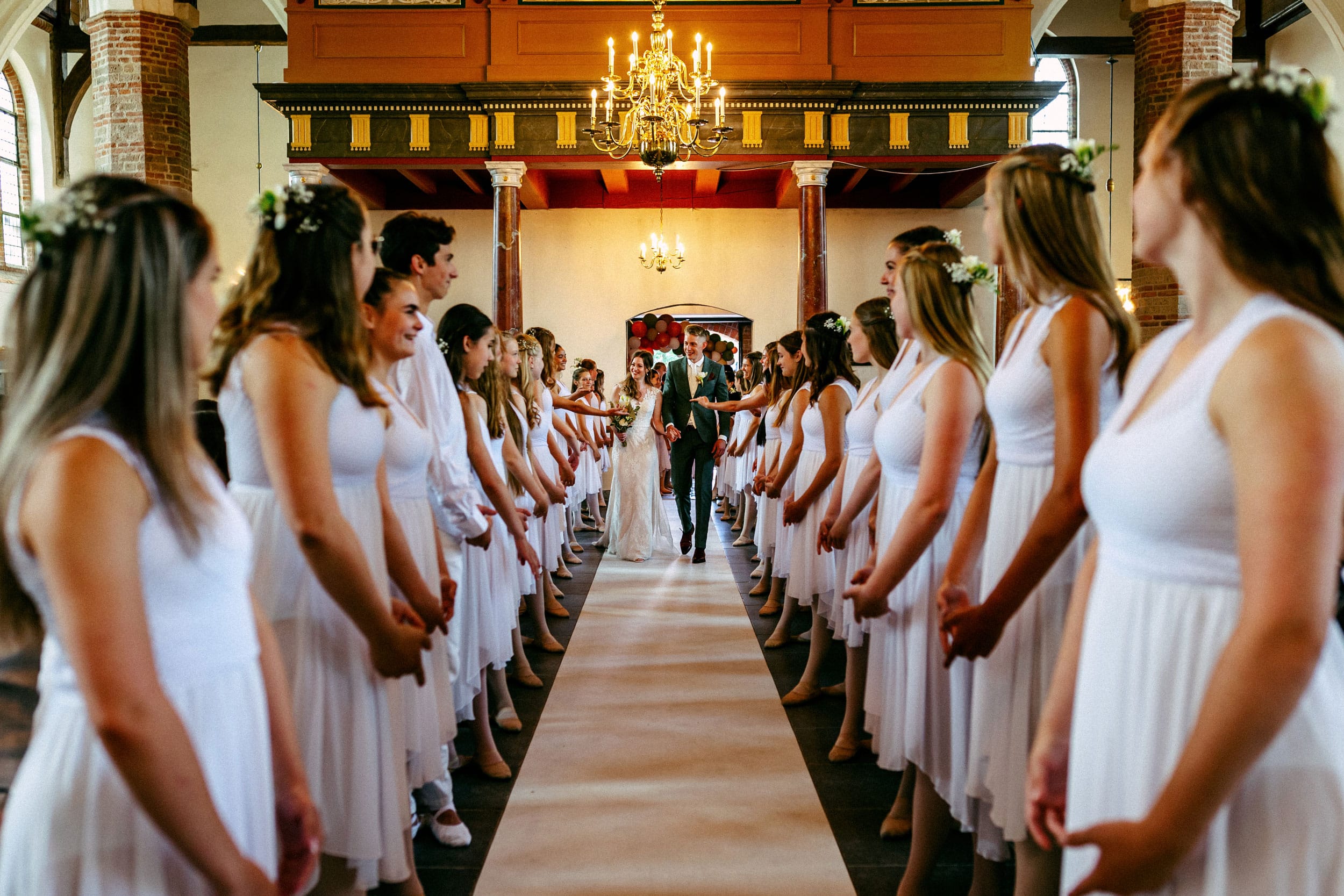 Een huwelijksceremonie in een kerk met bruidsmeisjes die door het gangpad lopen.
