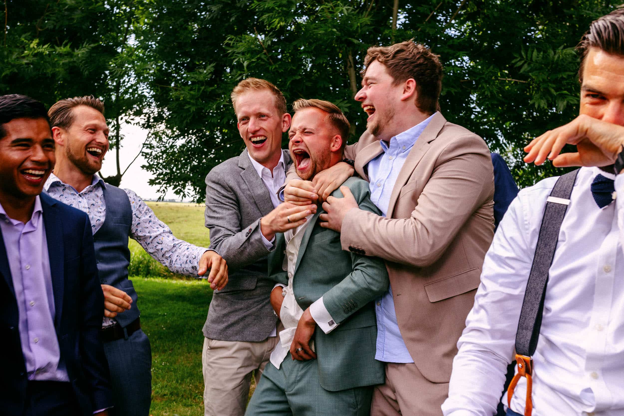 Een groep mannen die lachen terwijl ze stijlvolle trouwkleding dragen.