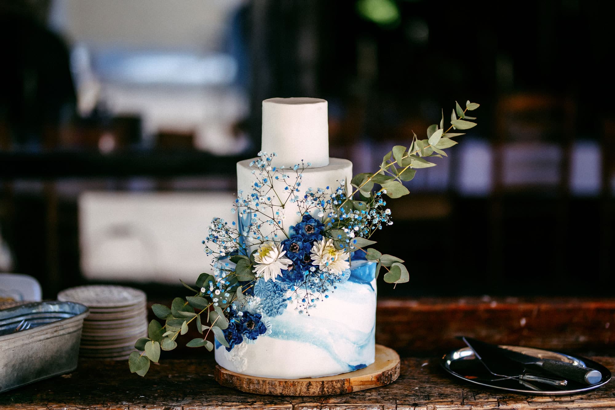A wedding cake of blue and white stands on a wooden table.