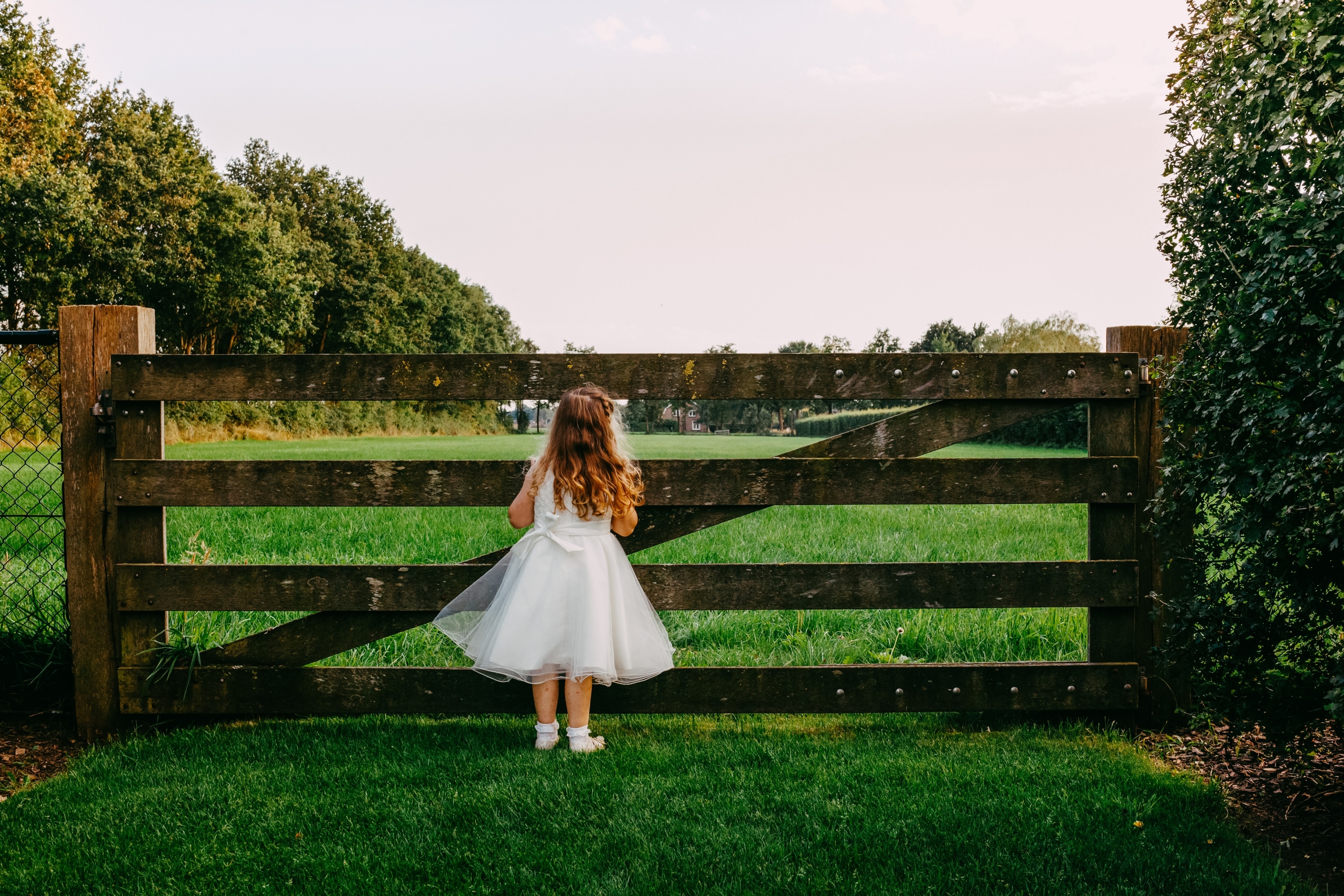 A girl standing by a fence, relaxing on the grass at a wedding.