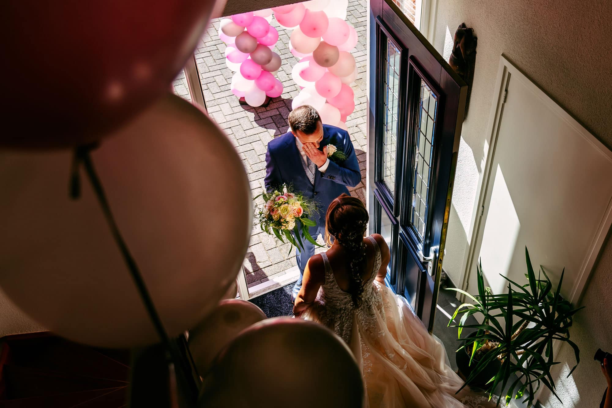 A bride and groom stand in front of balloons.