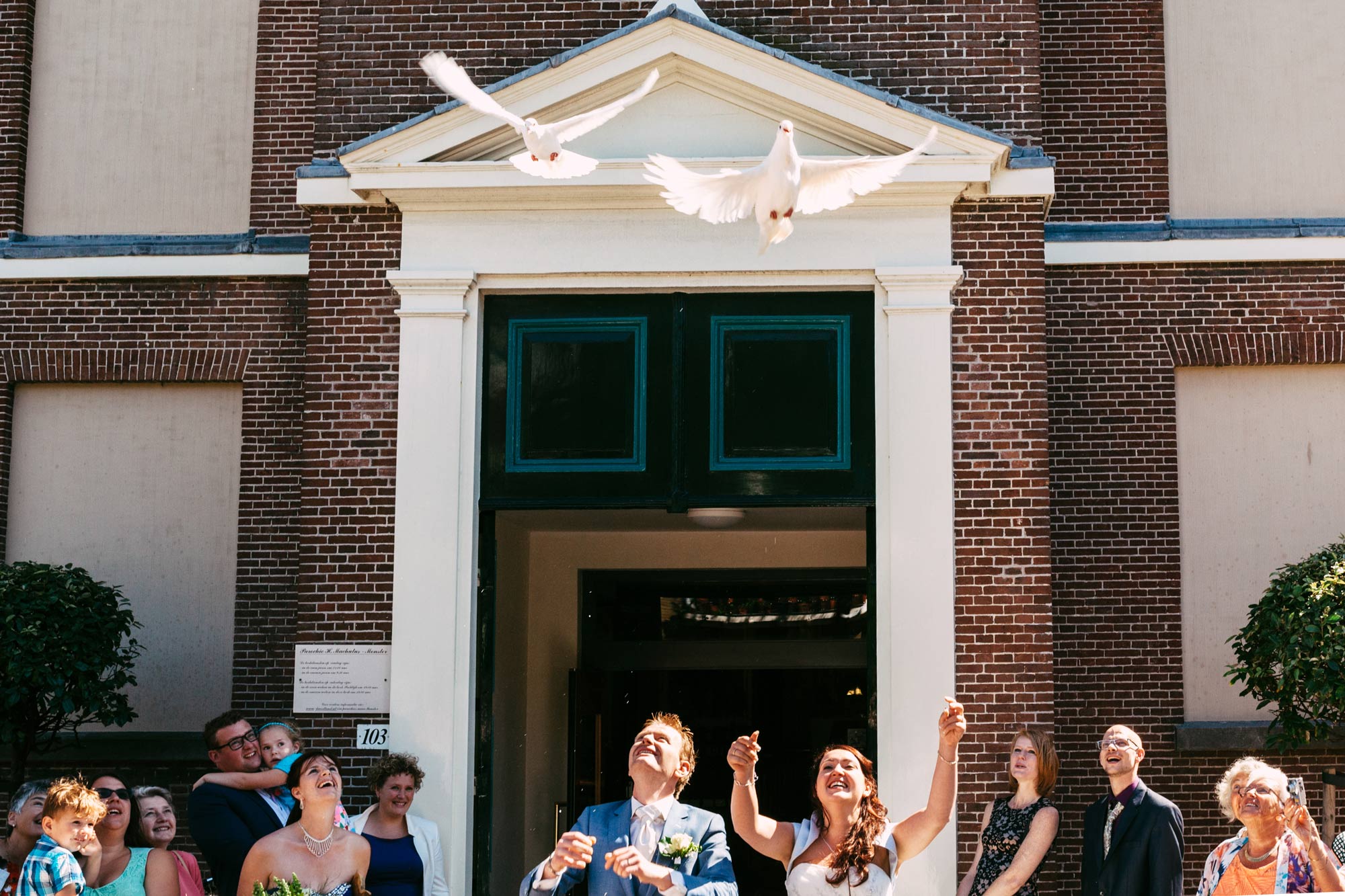 Een Nederlands bruidspaar gooit tijdens hun bruiloft duiven voor een kerk.