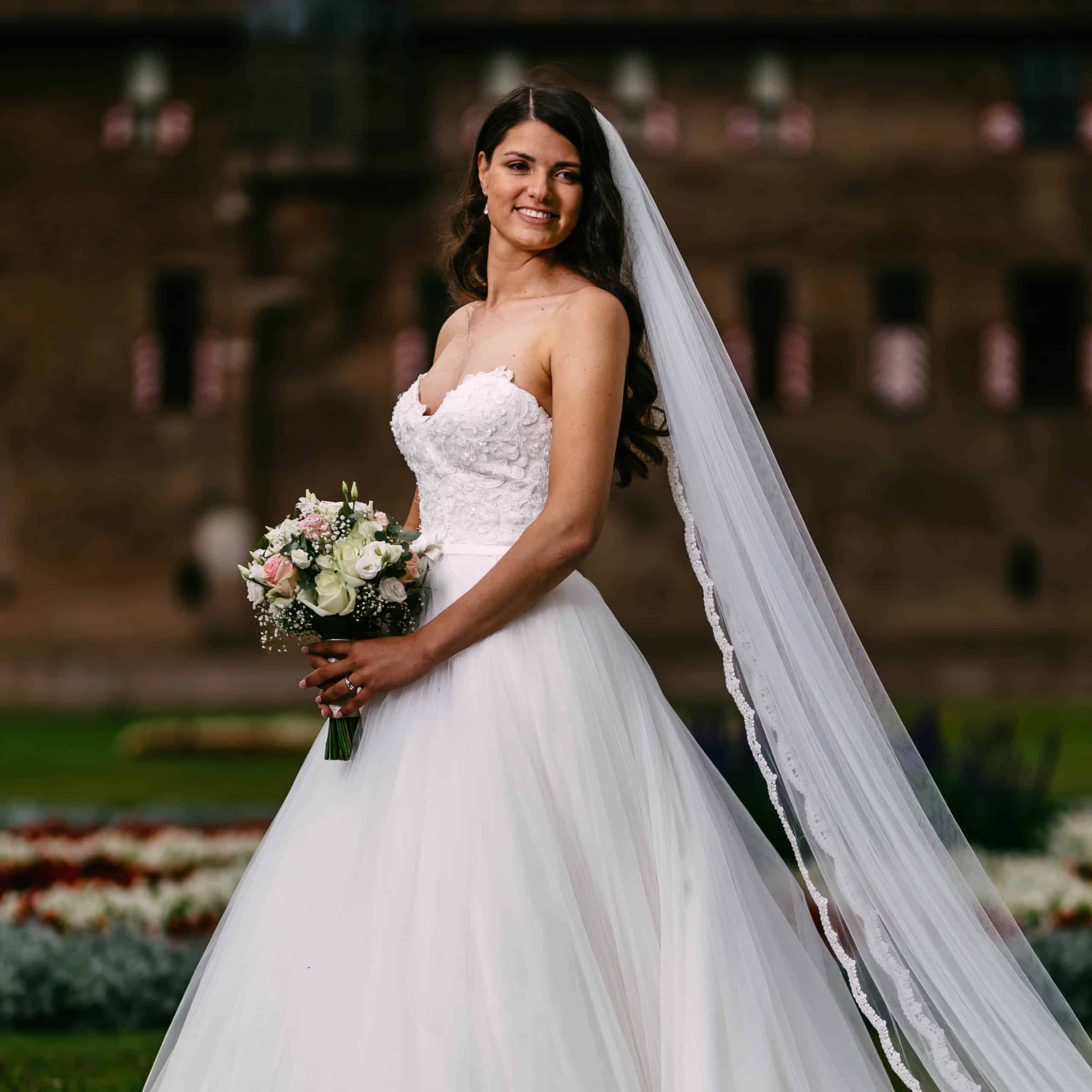 A bride in wedding dress stands in front of Castle de Haar.
