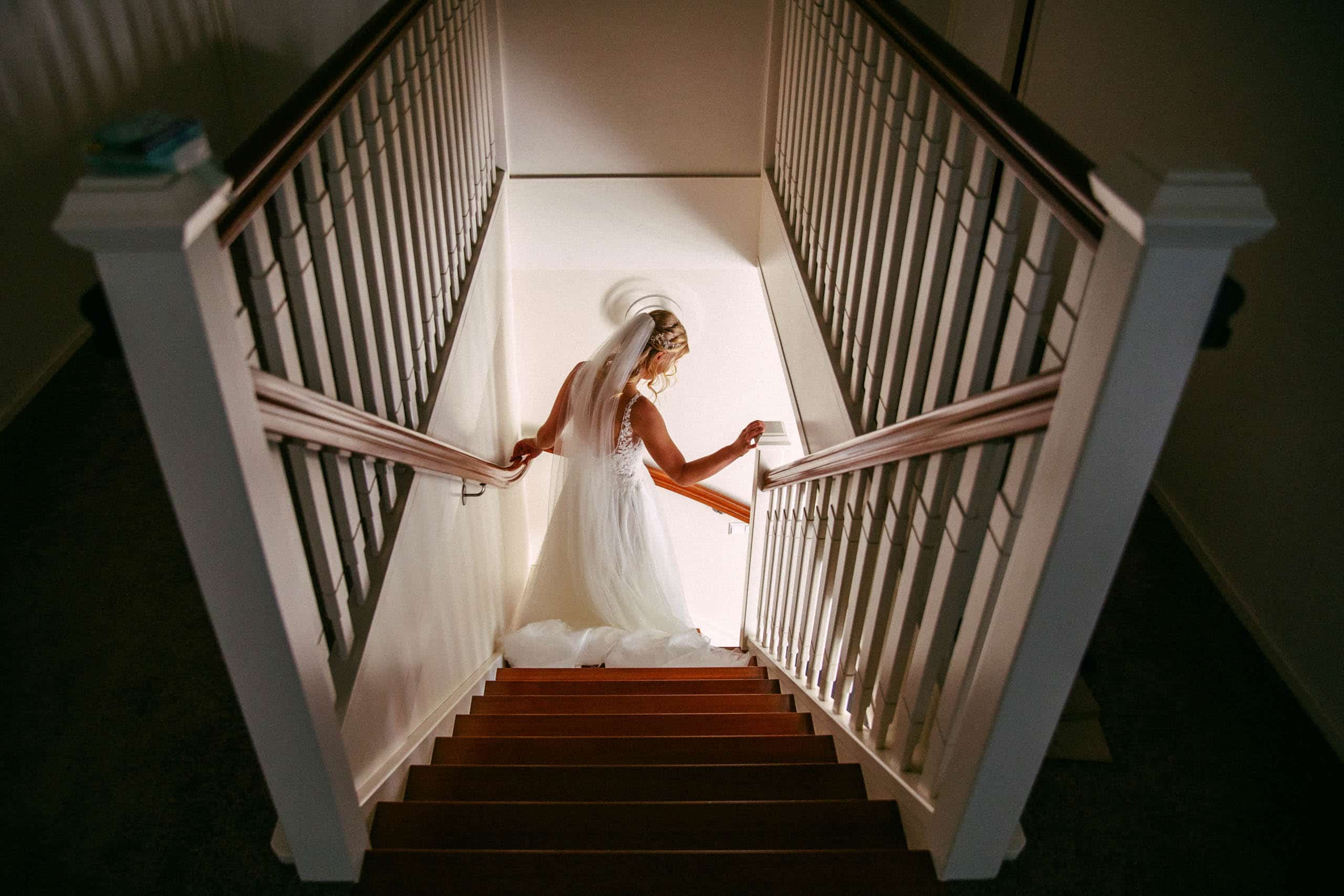Een bruid loopt sierlijk de trap af in haar trouwjurk, waardoor bijzondere trouwfoto's ontstaan.