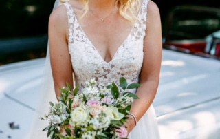 Een bruid in trouwjurk poseert naast een klassieke auto voor prachtige trouwfoto's.