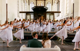 Een groep dansers in witte jurken treedt op in een kerk.