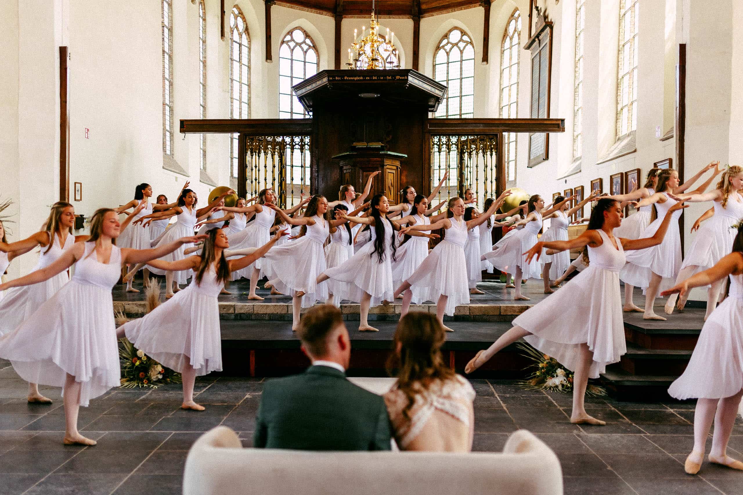Een groep dansers in witte jurken treedt op in een kerk.