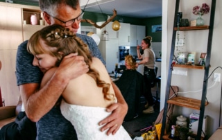 Een bruid omhelst haar vader in de woonkamer en legt een oprecht moment tussen hen vast op hun trouwdag.