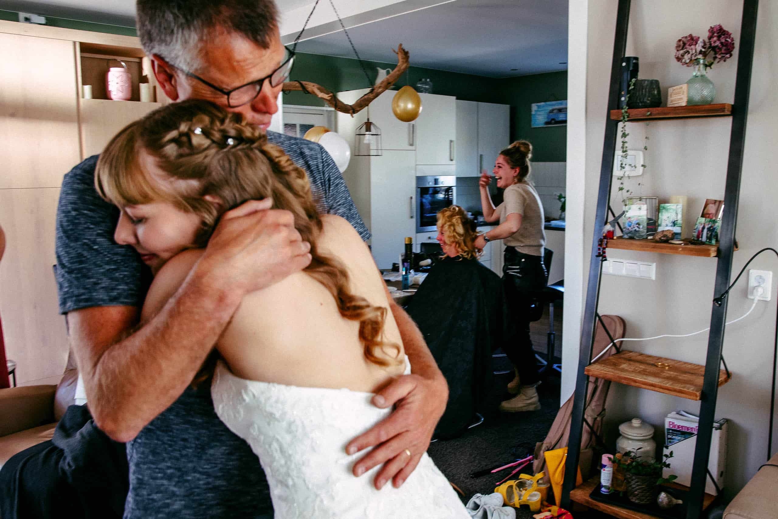 A bride hugs her father in the living room, capturing a heartfelt moment between them on their wedding day.