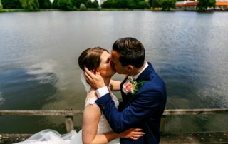 Trouwfoto's van een bruid en bruidegom die een romantische kus delen op een kade bij een meer.