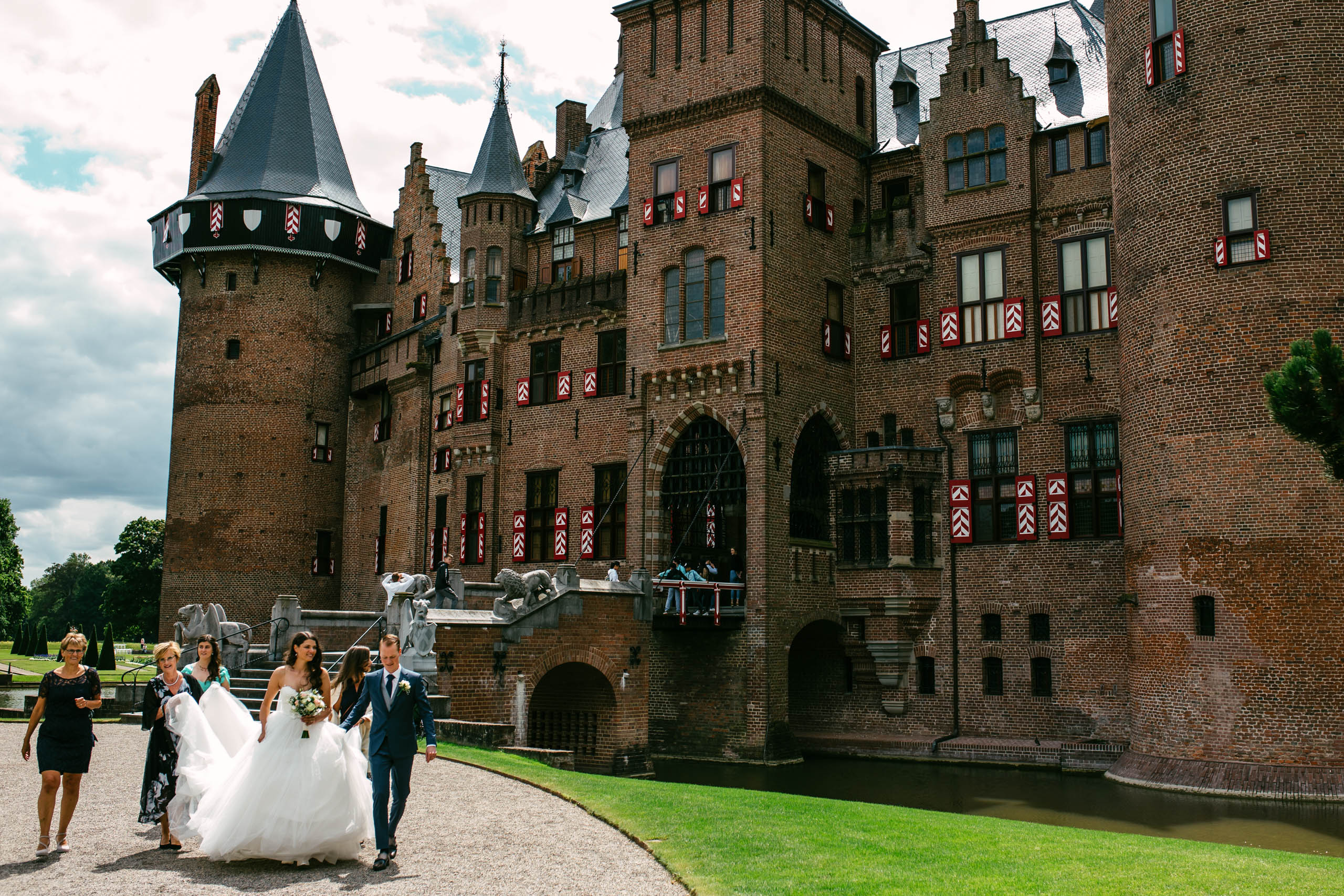 Een groep bruiden en bruidegommen loopt voor een kasteel en vinkt items af op hun trouwchecklist.