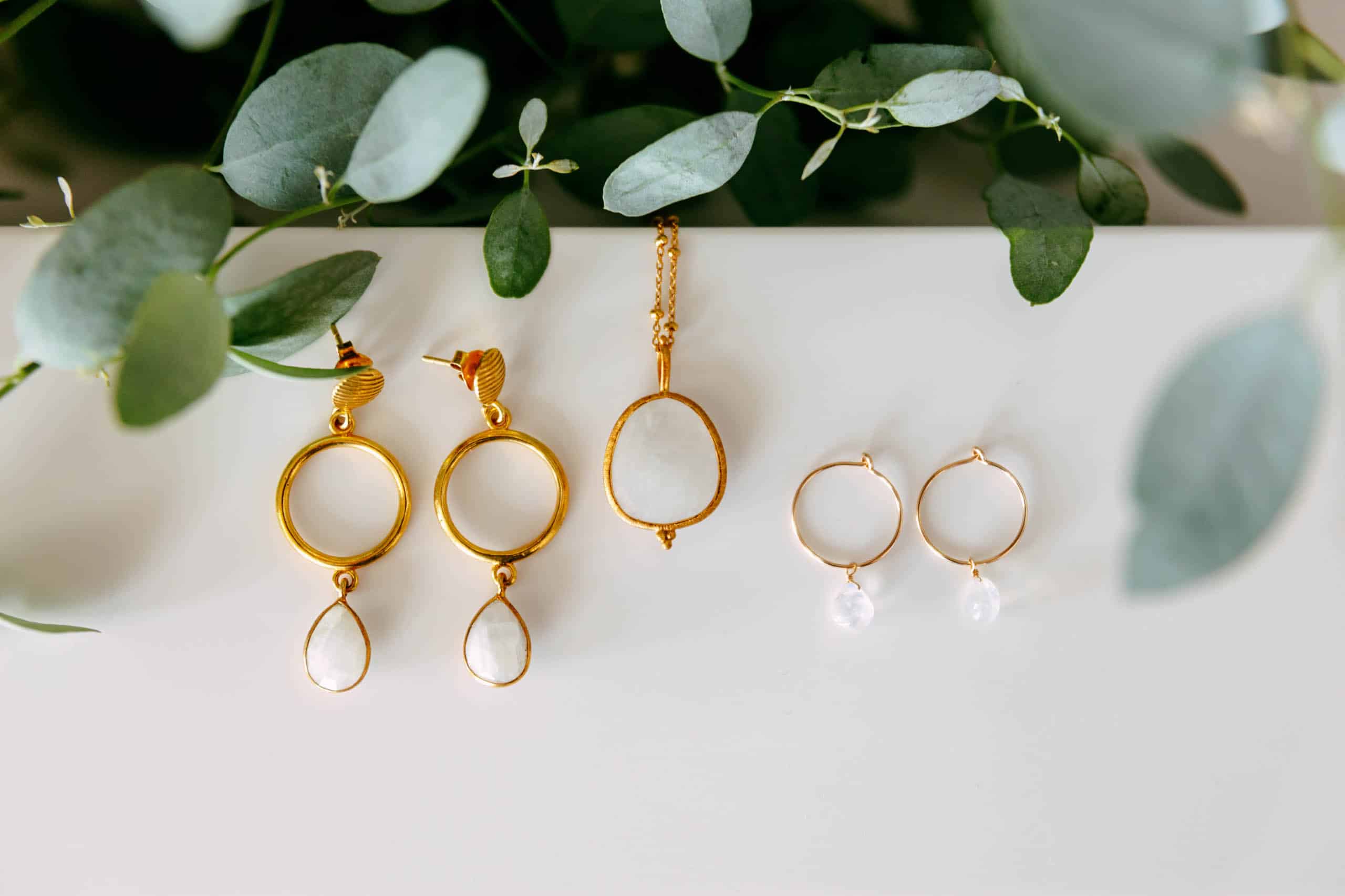 A white earring, a gold earring and a eucalyptus plant on a table as part of a wedding checklist.