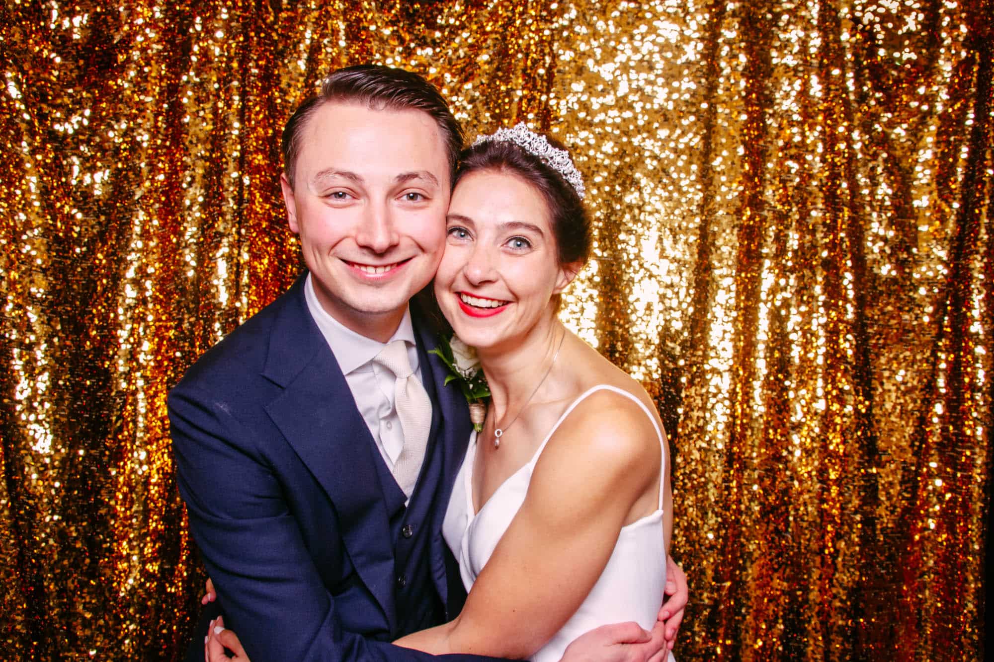 Een bruid en bruidegom in de photobooth, poserend voor een gouden achtergrond op hun bruiloft.
