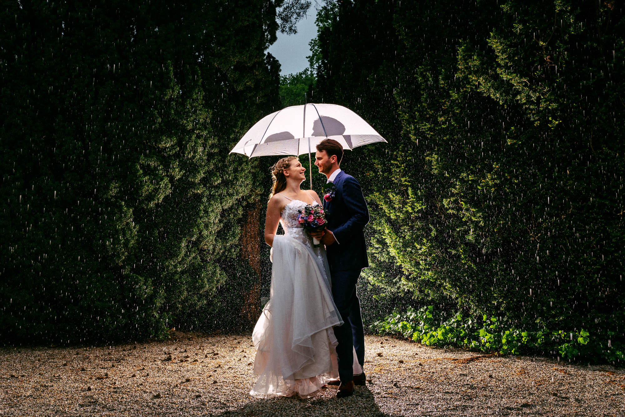 Regen op je bruiloft - Een bruid en bruidegom staan onder een paraplu in de regen.