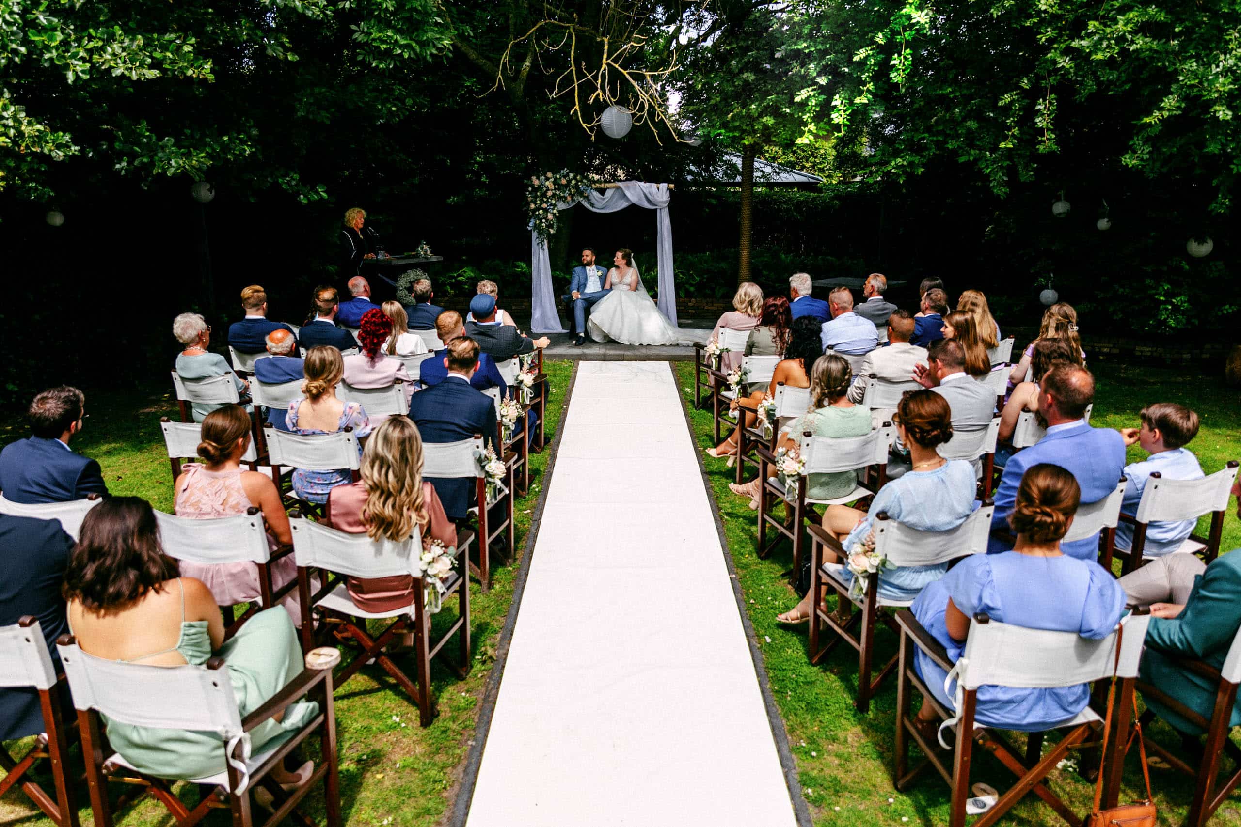 Een tuinhuwelijksceremonie waar mensen op stoelen zitten,
naast een handige Bruiloft checklist voor planningsdoeleinden.