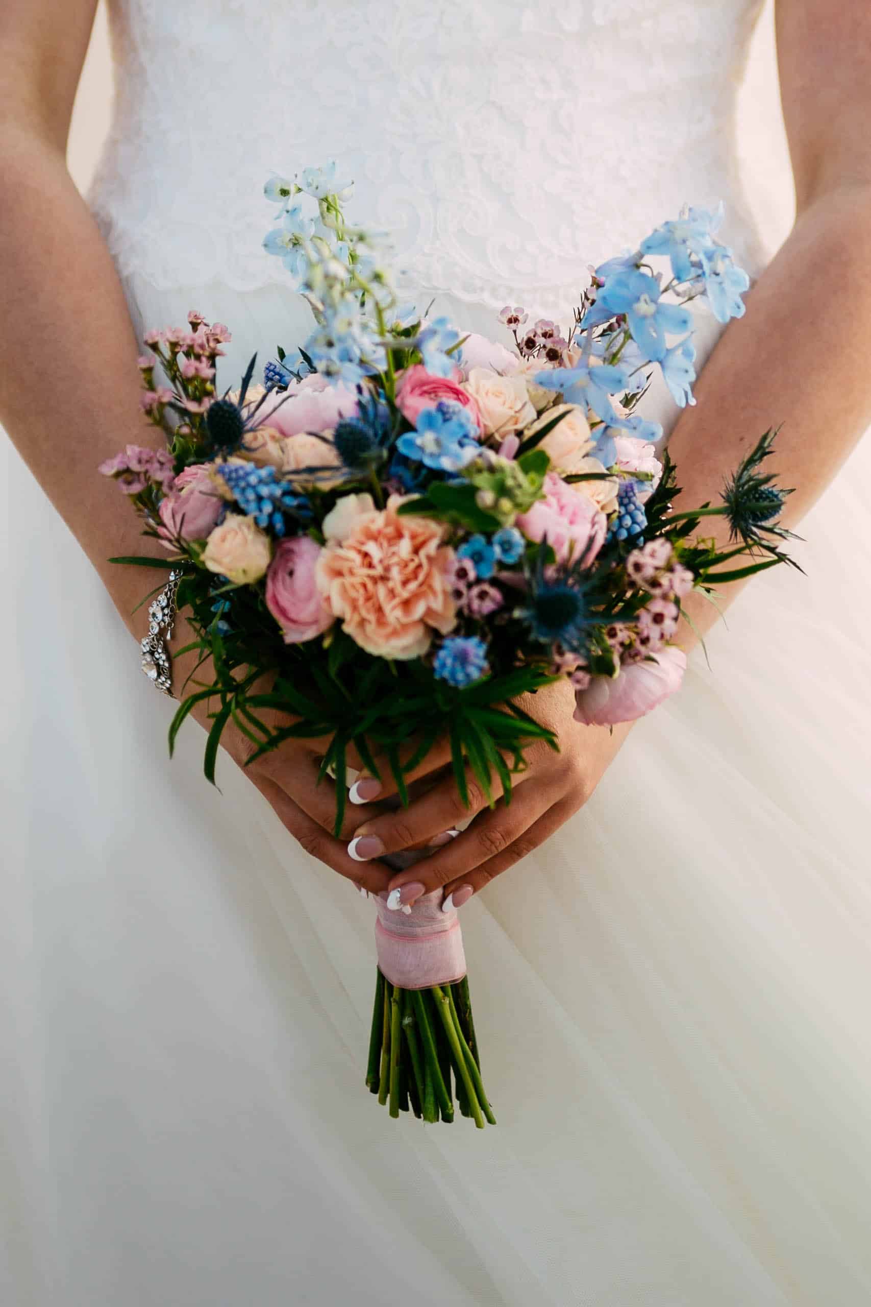A bride with a wedding bouquet of blue and pink flowers.