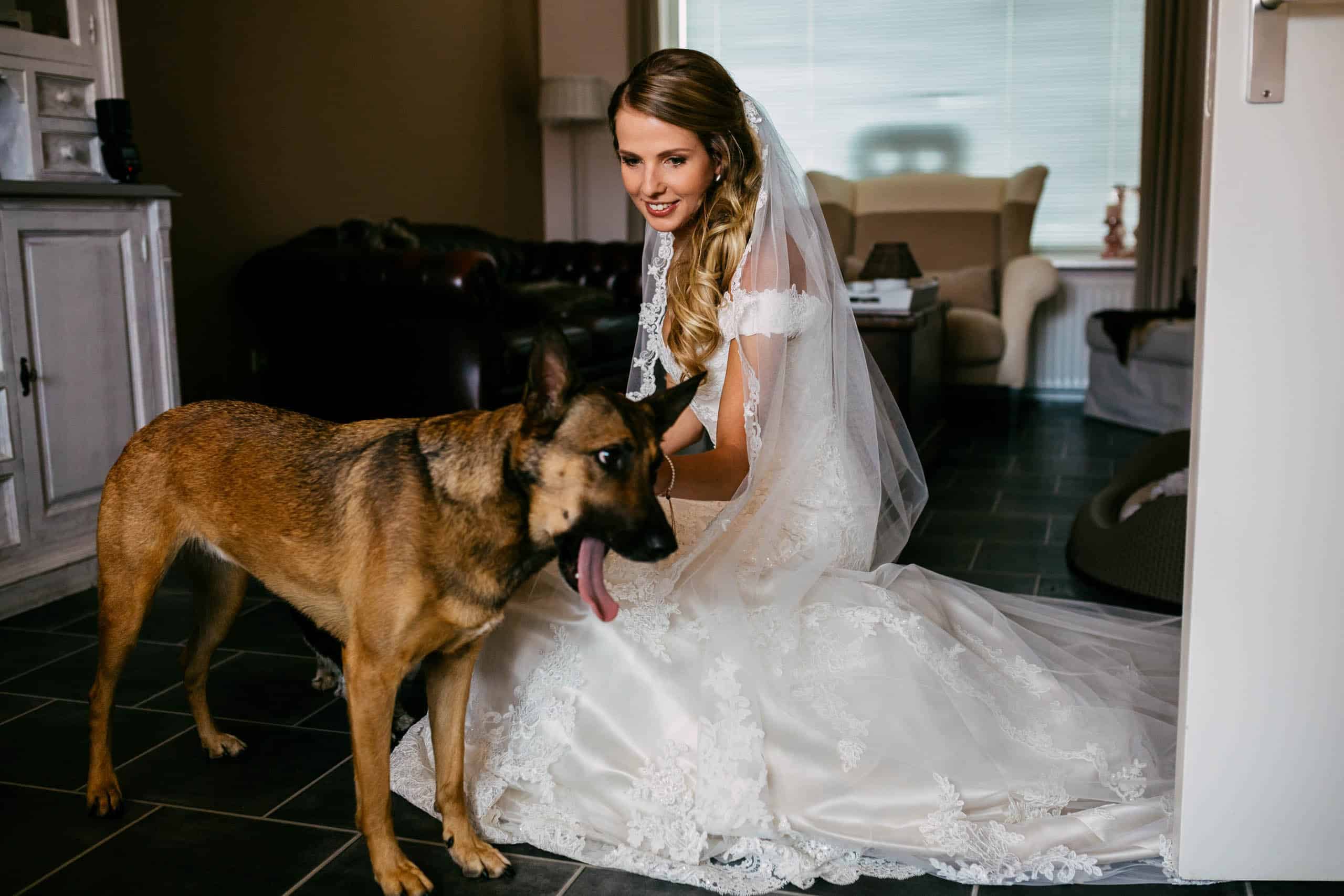 Een bruid in trouwjurk aait haar hond tijdens een dierenbruiloft.