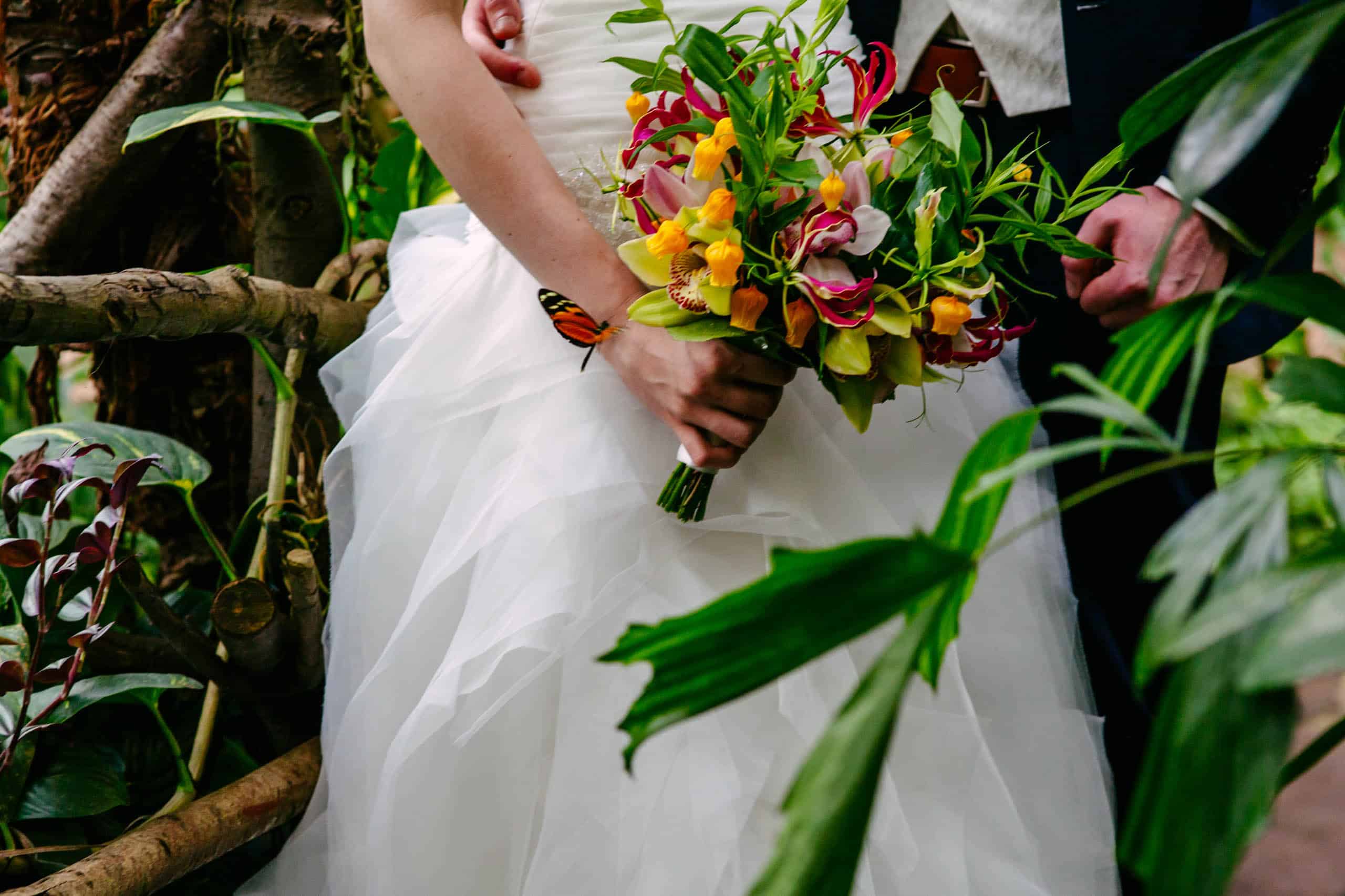 Een bruid en bruidegom presenteren een boeket in een schilderachtige tropische omgeving.