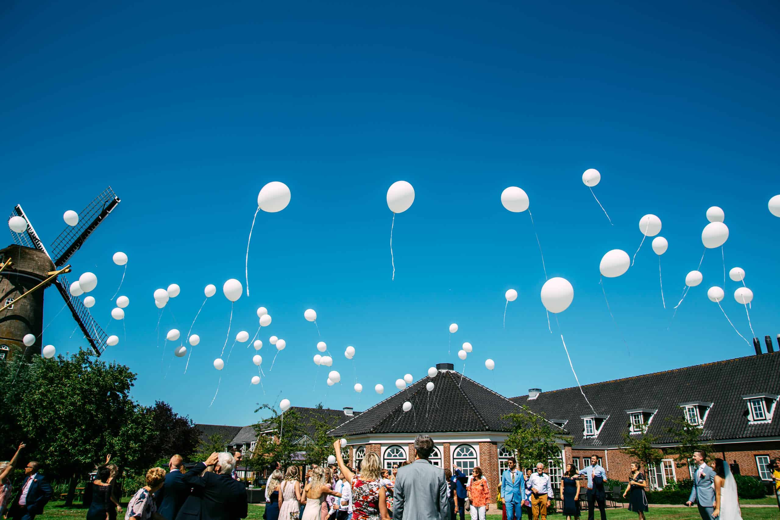 Witte ballonnen zweven in de lucht voor een Nederlandse windmolen op een vreugdevolle bruiloft.