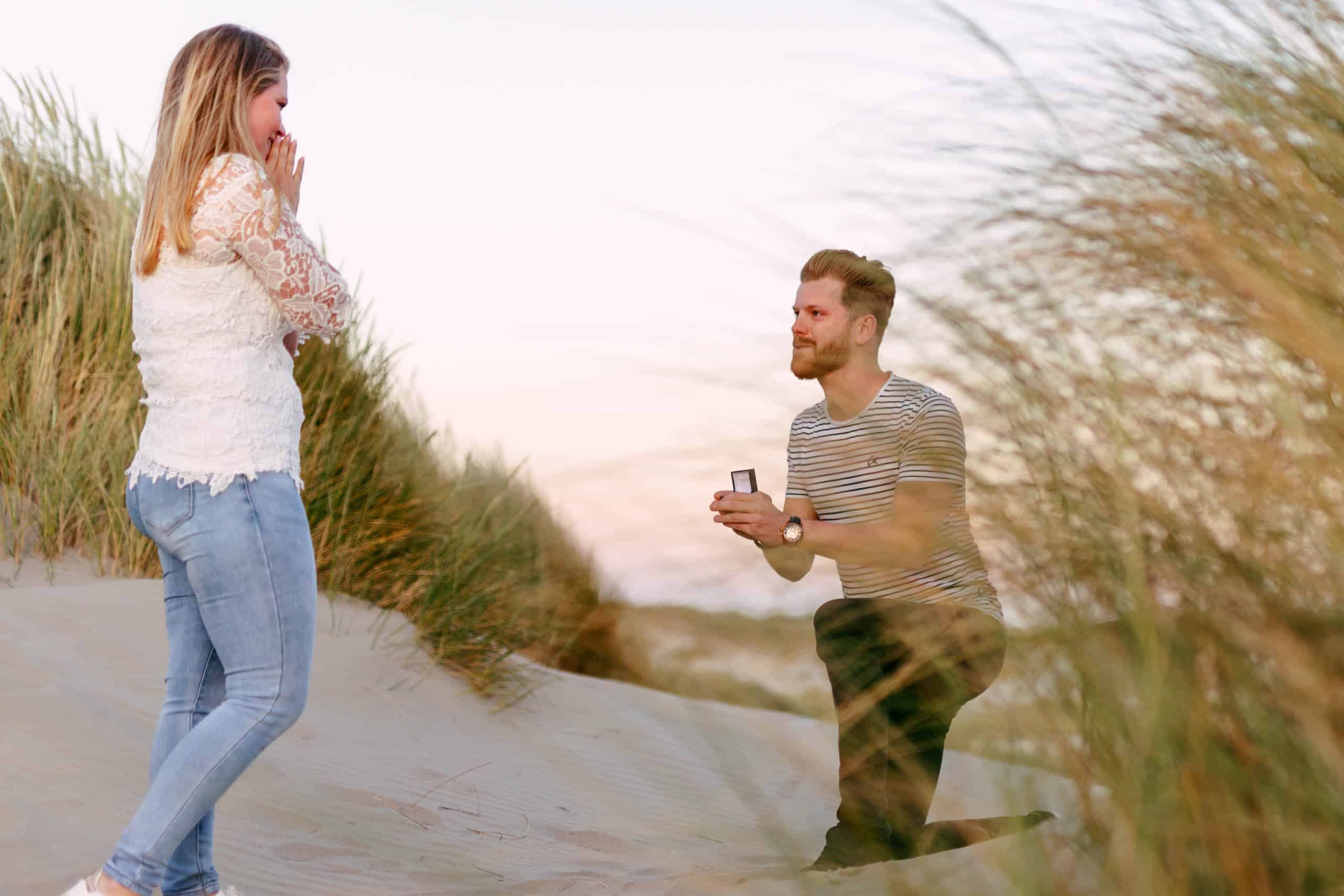 Een man doet een vrouw in het zand een aanzoek en vraagt haar tien ten huwelijk.
