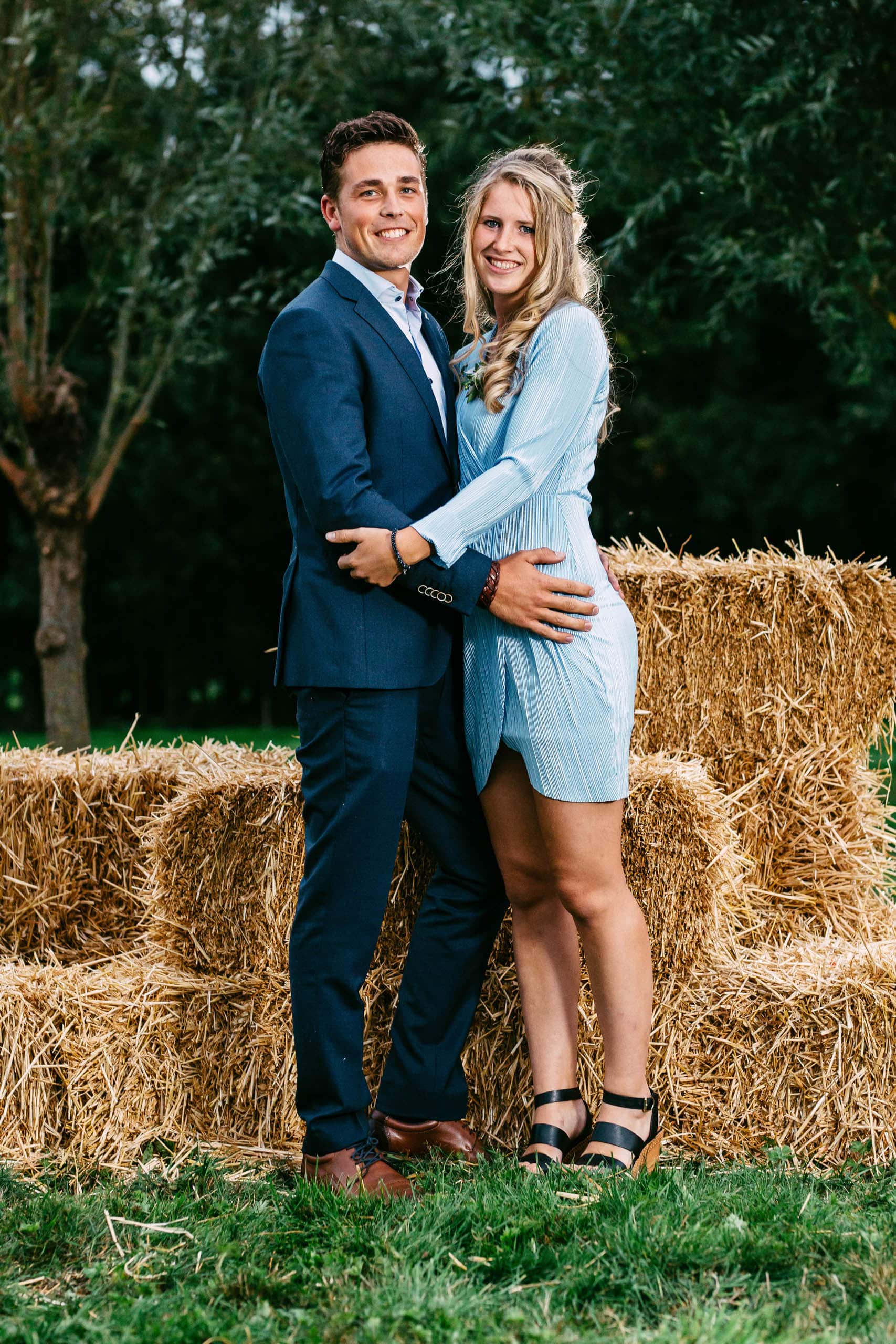 A couple posing elegantly in front of hay bales, showing off their impeccable 'tenue de ville' style.
