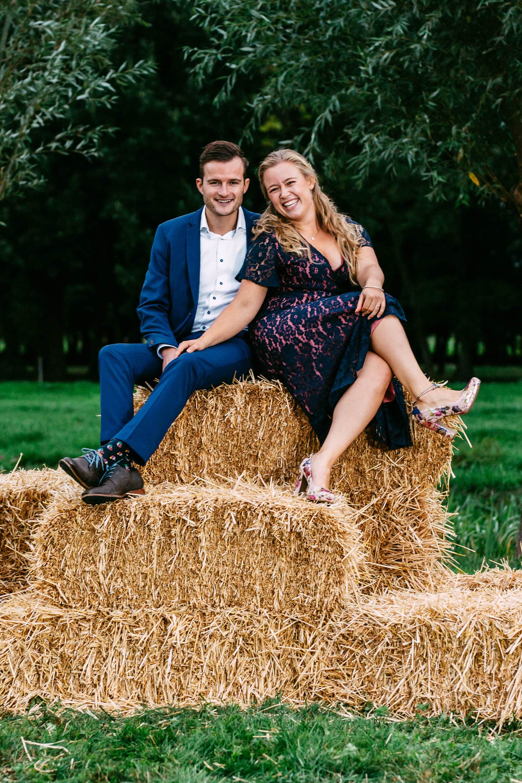 A couple sitting in a field on hay bales, dressed in Tenue de ville attire.
