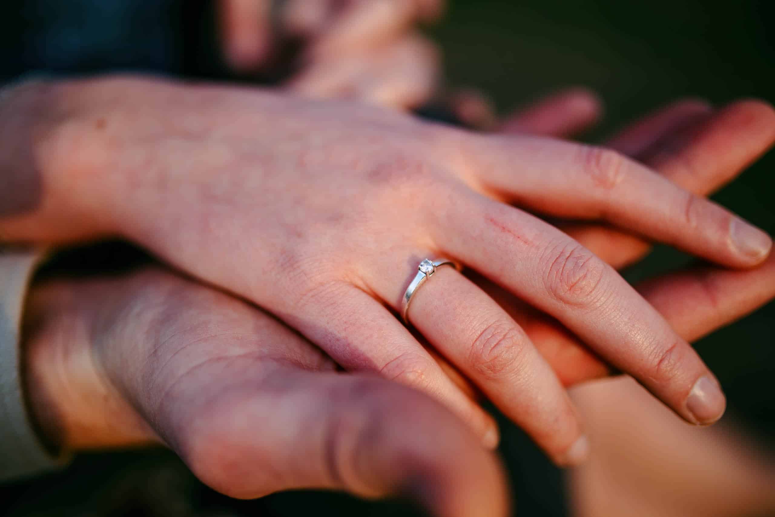 De handen van een stel houden een verlovingsring vast tijdens een romantisch aanzoek.