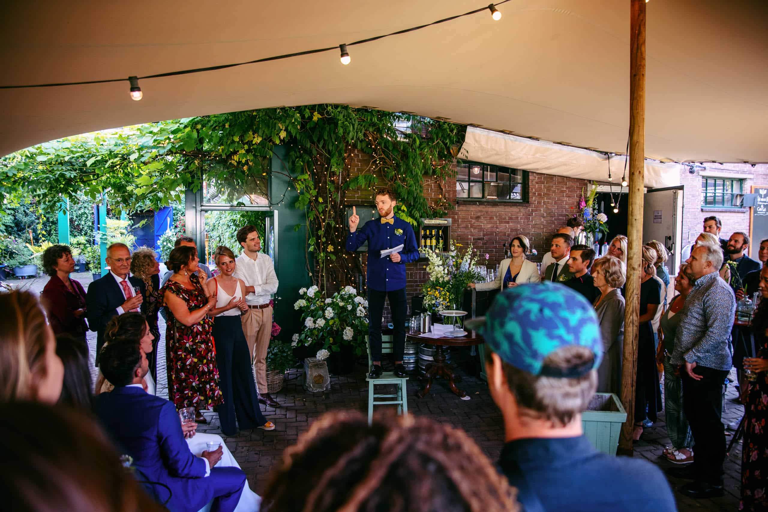 A man gives a speech at a Dutch wedding to a crowd of people.