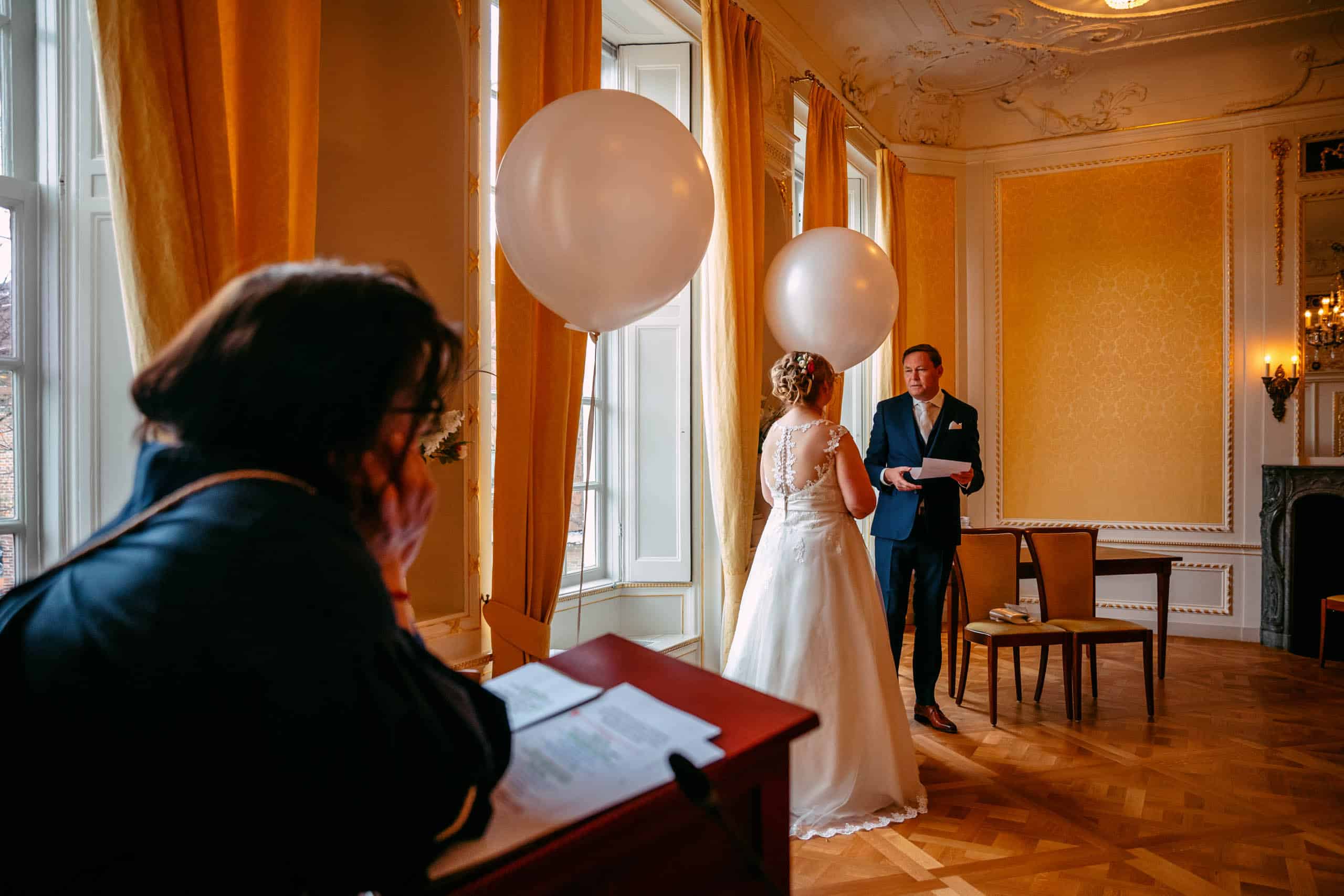 A bride and groom stand in a room decorated with balloons before their wedding.