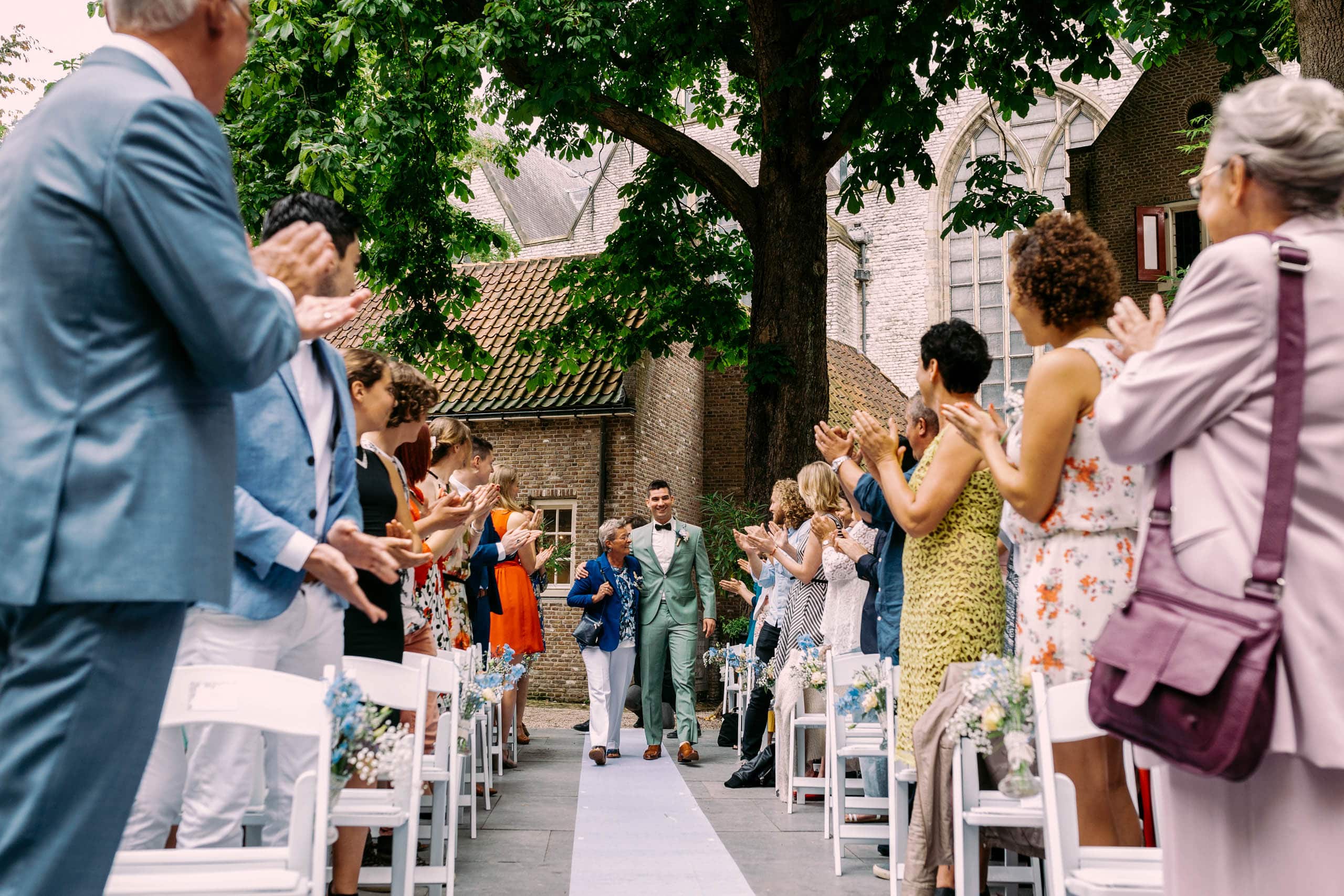 Een huwelijksceremonie op een binnenplaats met applaudisserende mensen.